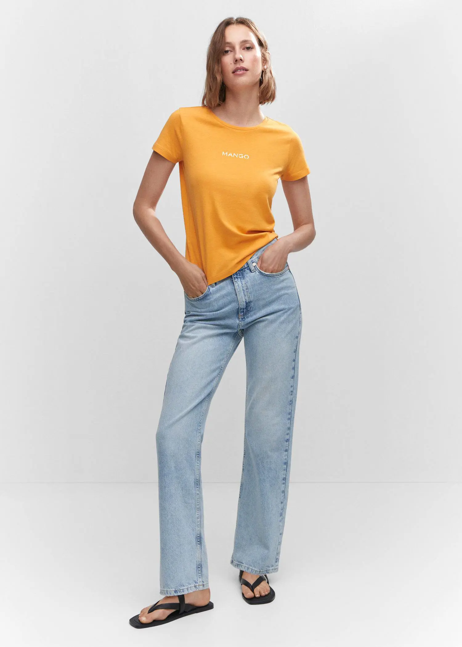 Mango Metallic logo T-shirt. a woman in a yellow shirt and blue jeans. 