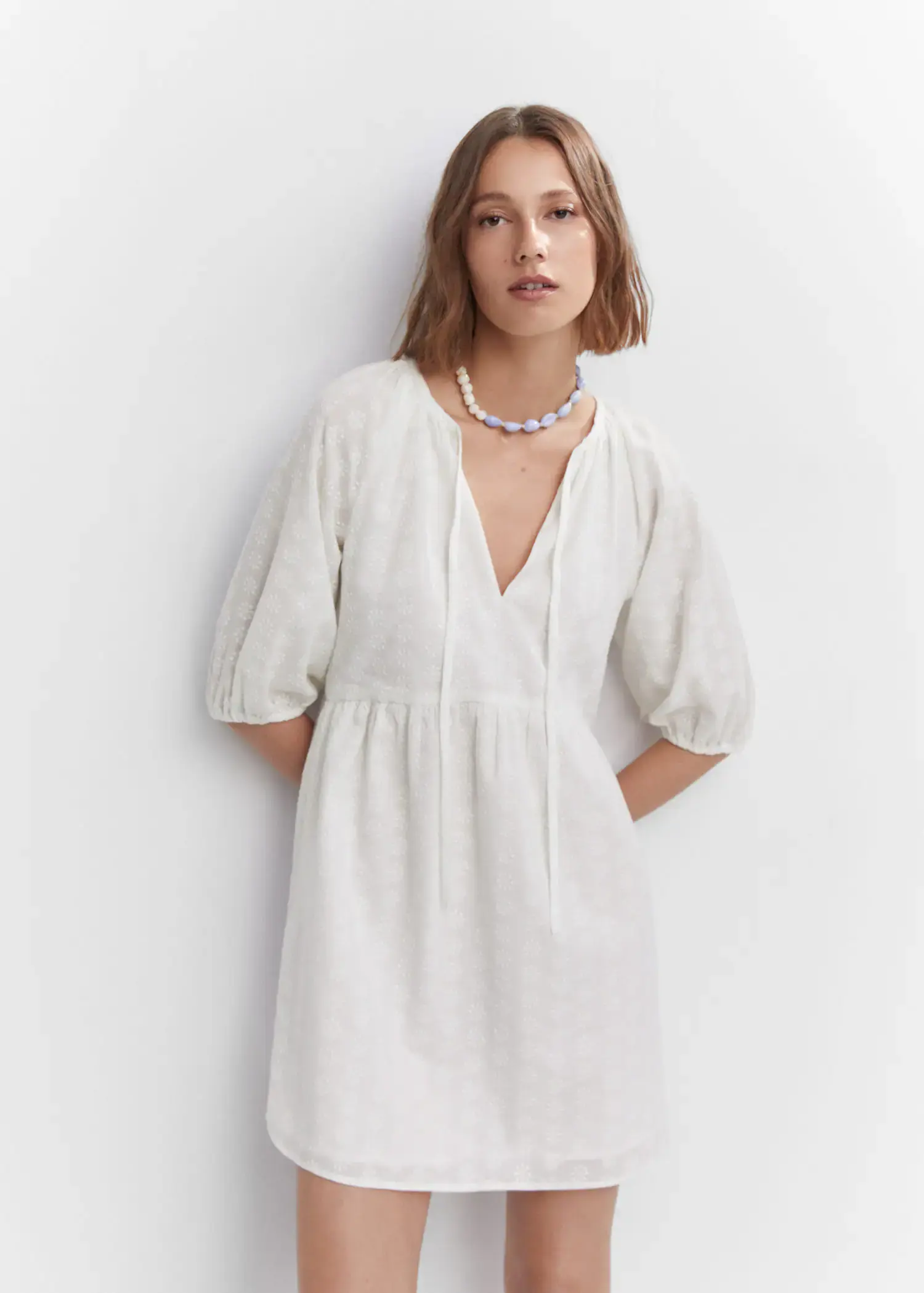 Mango Puff-sleeved embroidered dress. a woman wearing a white dress standing next to a wall. 