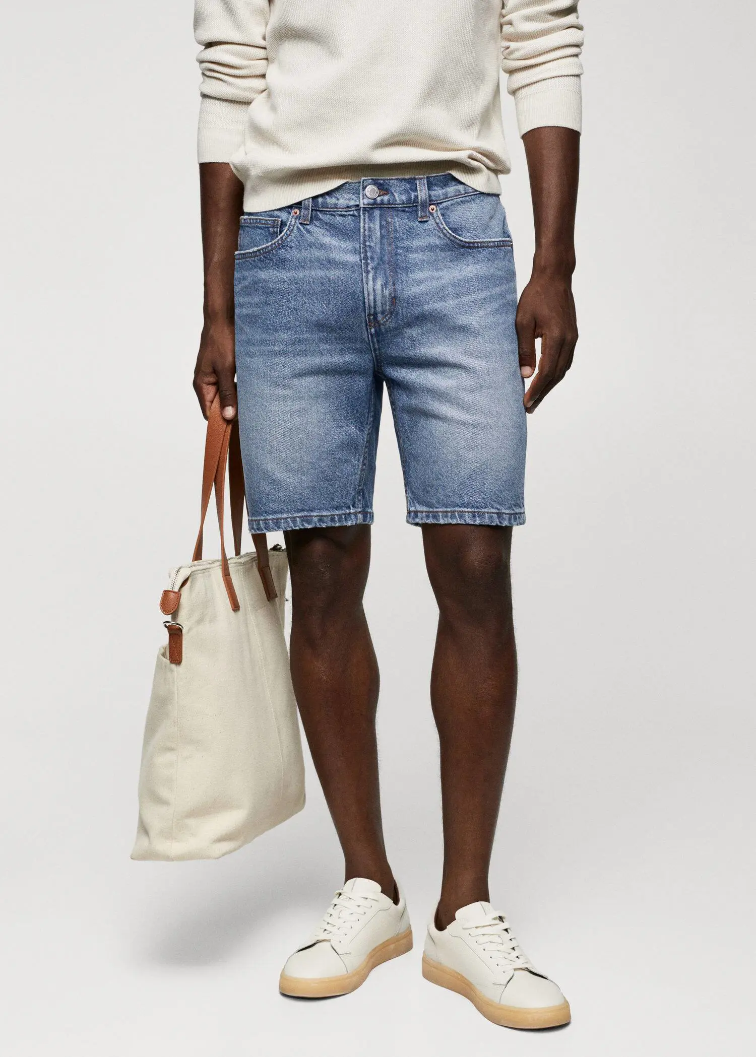 Mango Regular-fit denim bermuda shorts. a man holding a bag while standing next to his shorts. 