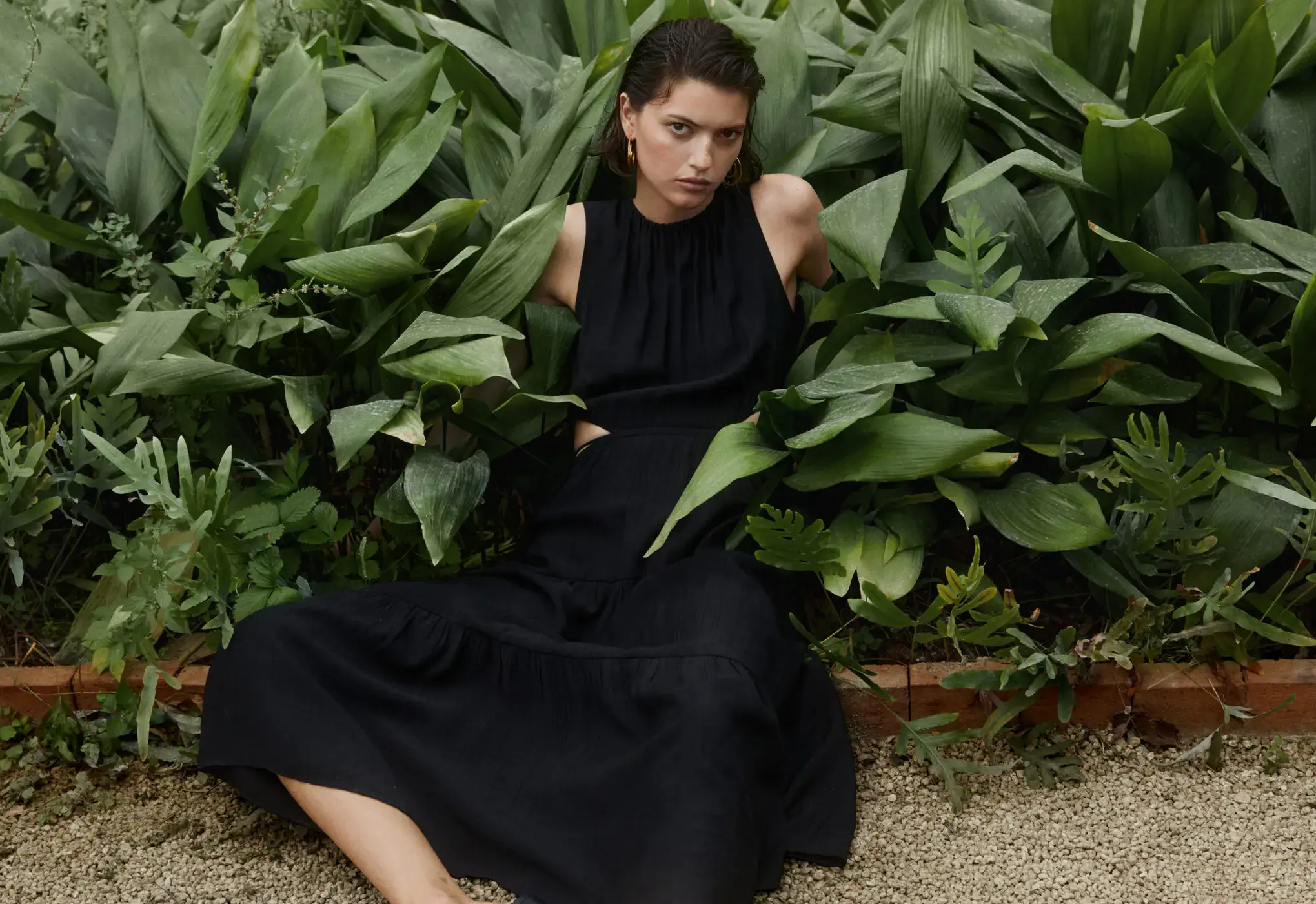 Mango Flared dress with openings. a woman in a black dress sitting in a garden. 