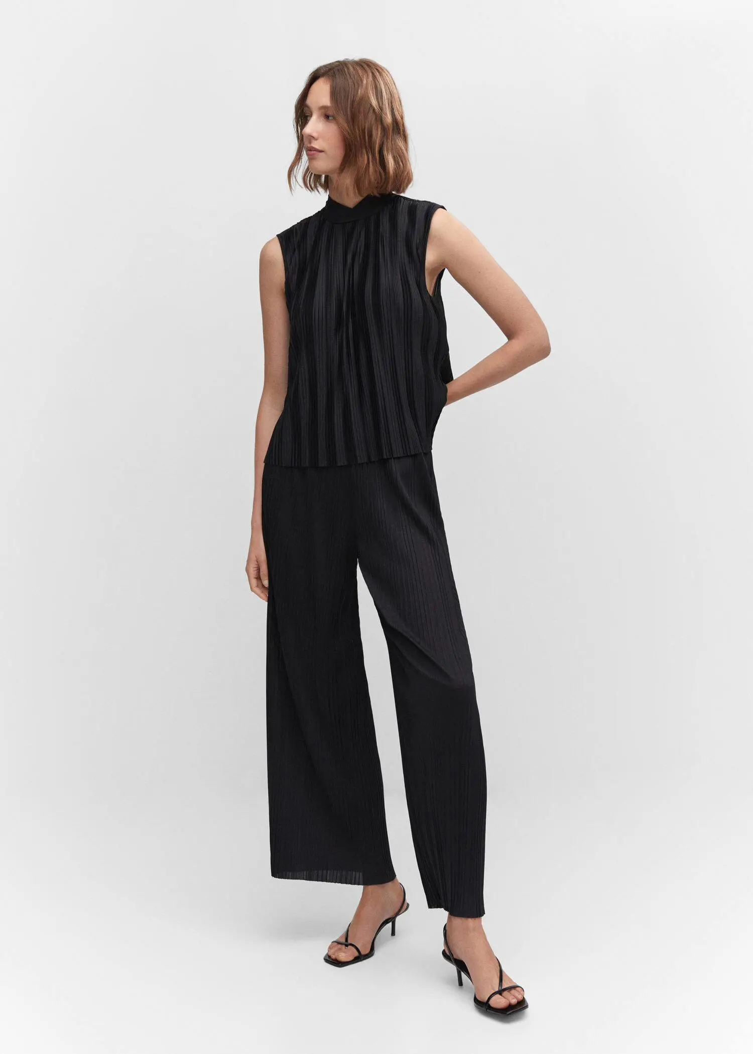 Mango Pleated bow top. a woman in a black outfit standing in front of a white wall. 