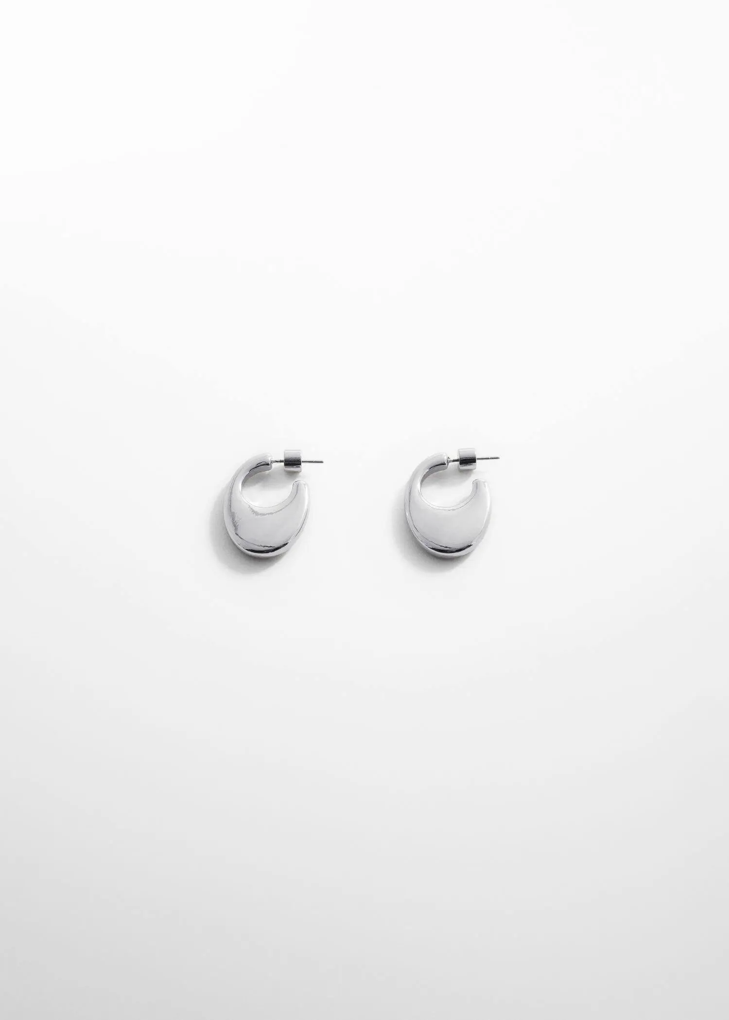 Mango Oval hoop earrings. a pair of silver earrings on a white wall. 