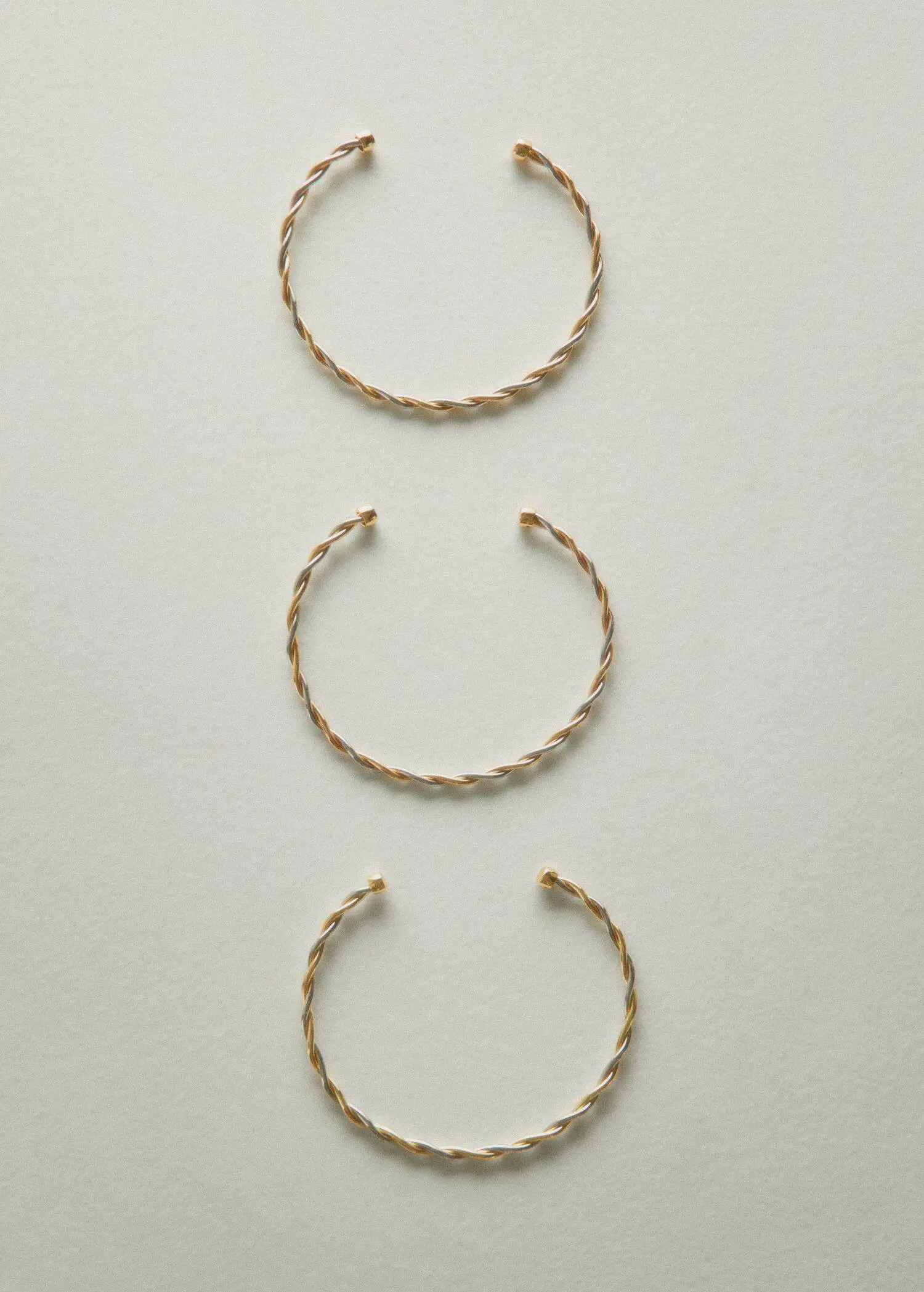 Mango Criss-cross rigid necklace. three bracelets are shown on a white surface. 