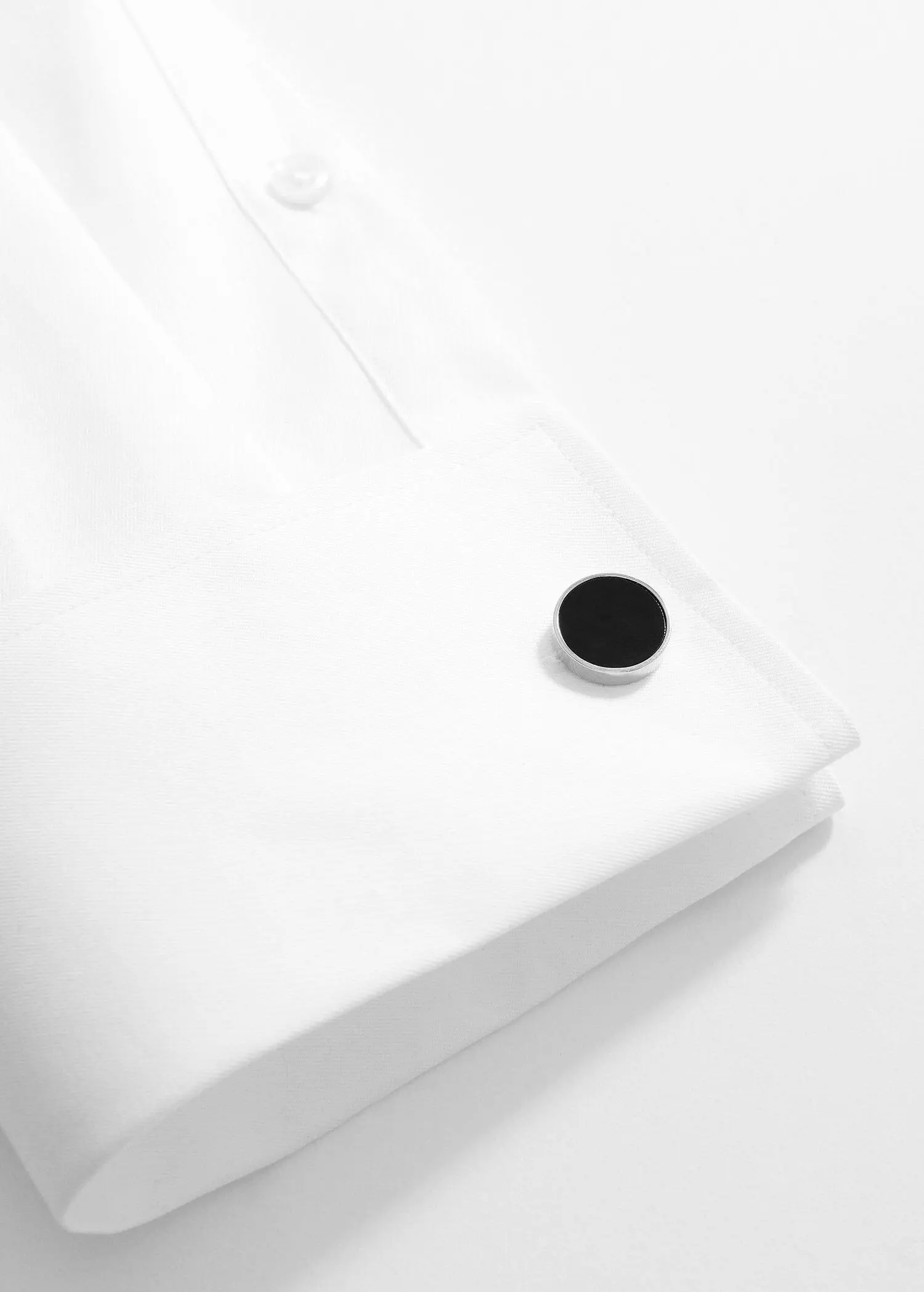 Mango Round black cufflinks. a button on a white shirt on a table. 