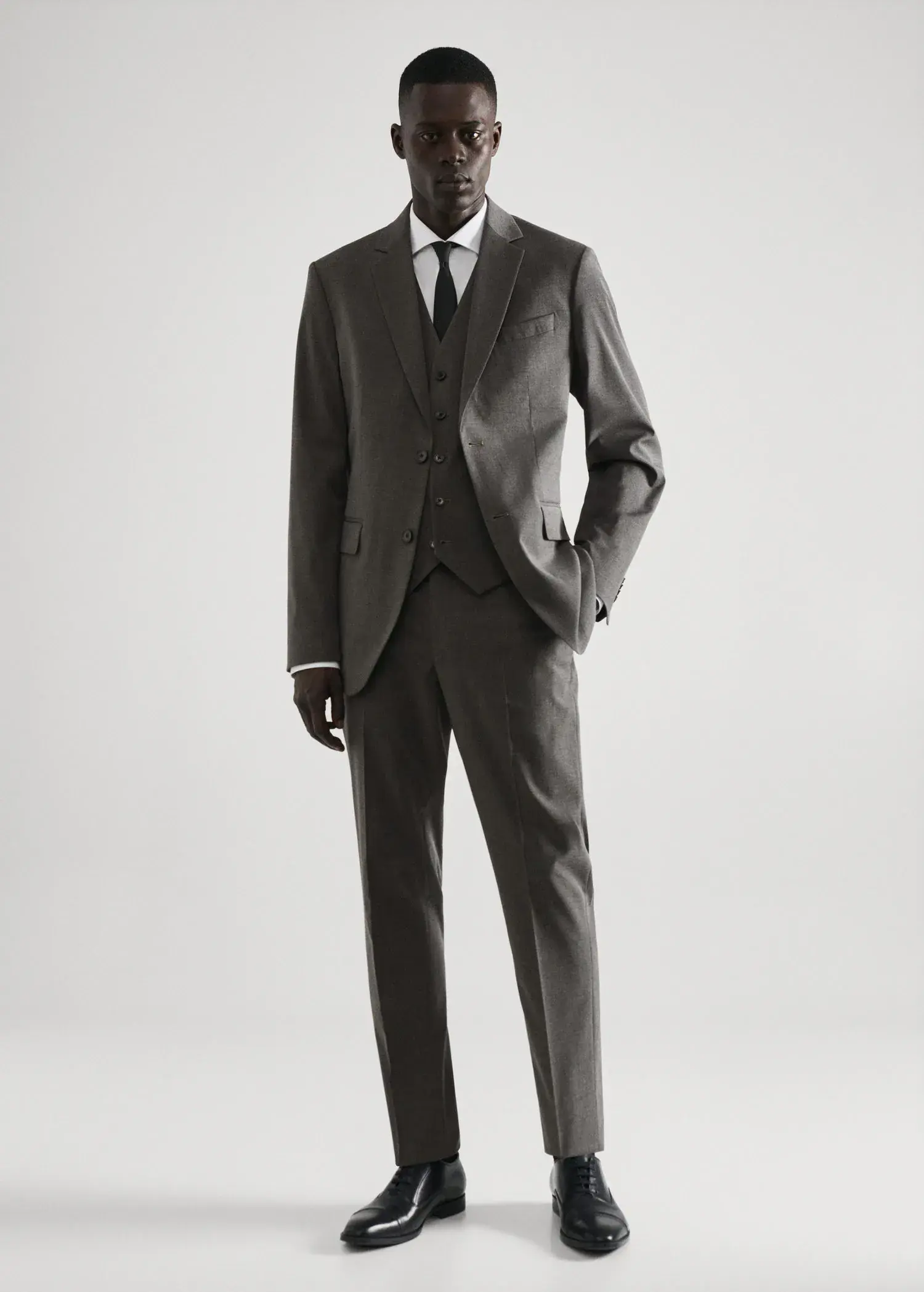 Mango Slim-fit suit waistcoat. a man wearing a suit and tie standing in front of a white wall. 
