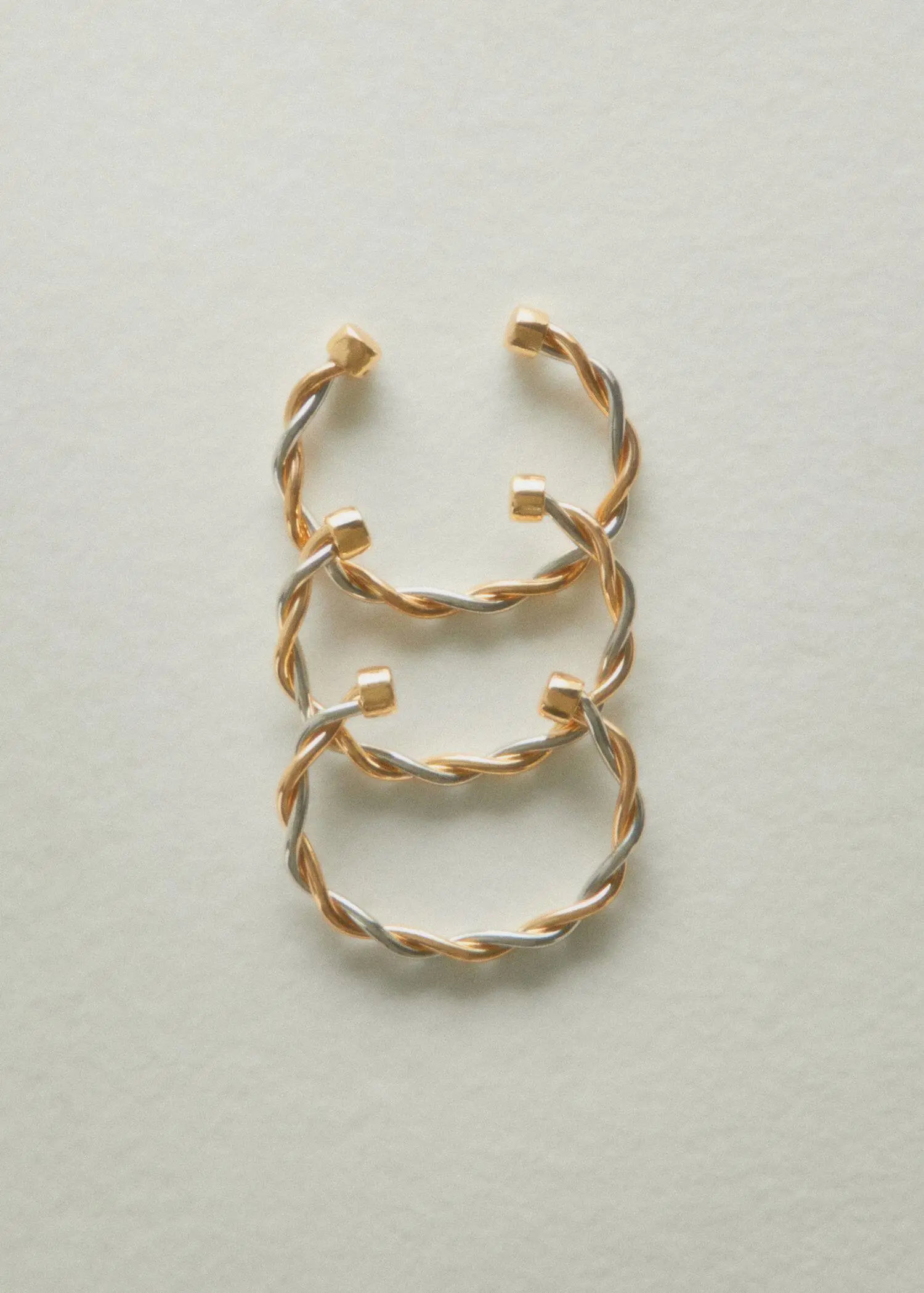 Mango Rigid interlocking bracelet. three pairs of gold and silver bangles on top of a white surface. 
