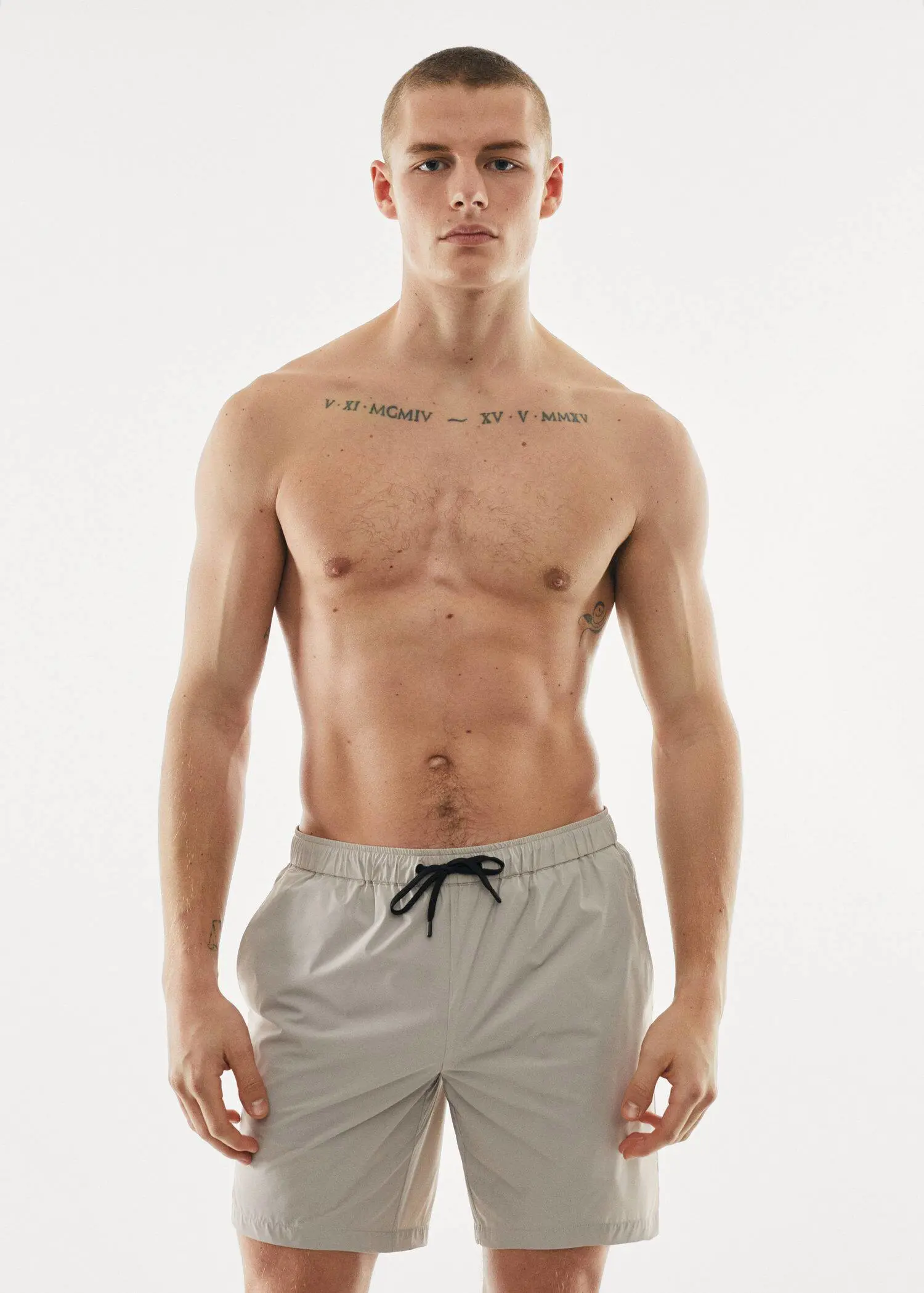 Mango Cord plain swimming trunks. a shirtless man in white shorts standing in front of a wall. 