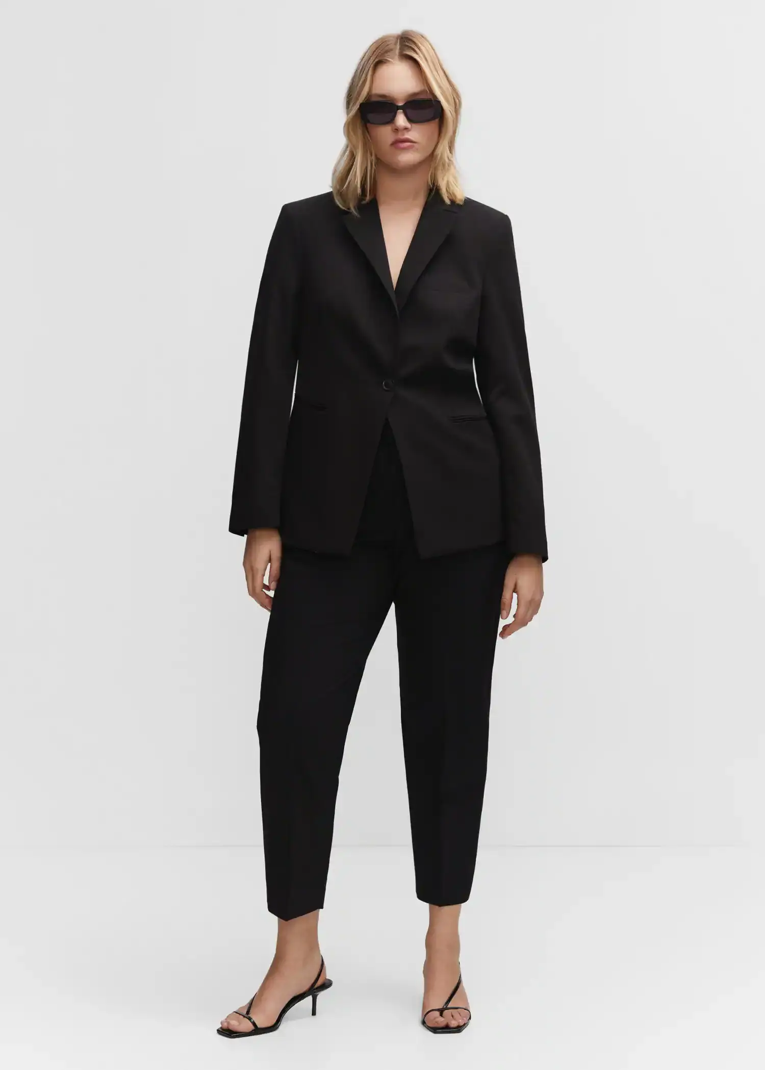 Mango Fitted suit blazer. a woman wearing a black suit standing in front of a white wall. 