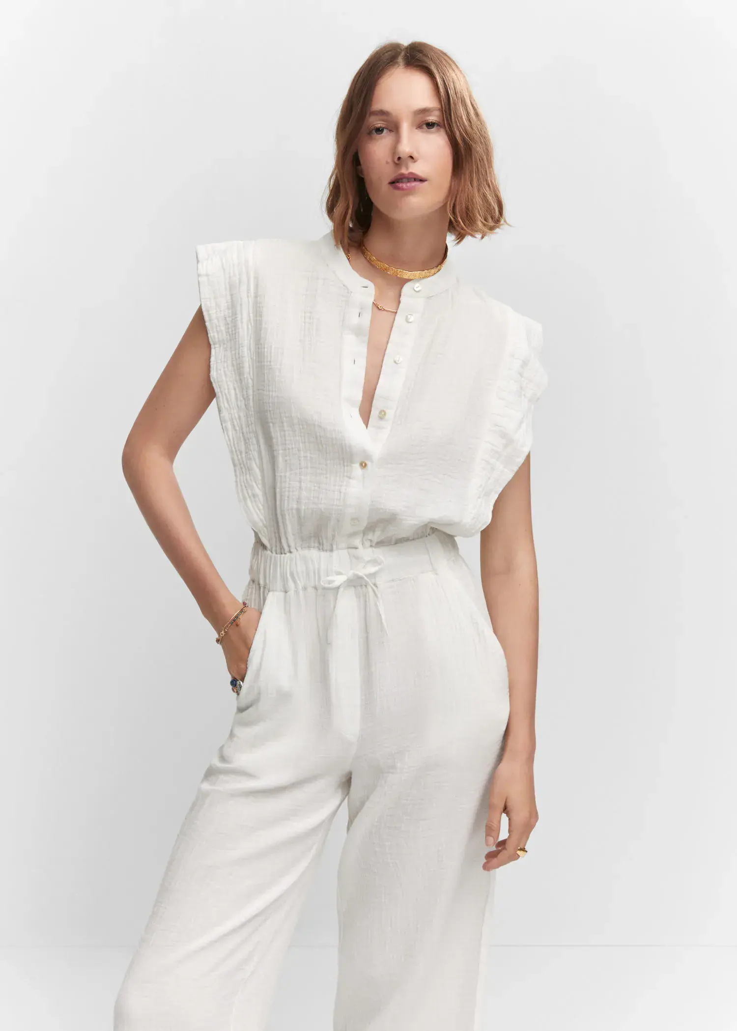 Mango Textured jumpsuit with button. a woman wearing a white jumpsuit and a gold necklace. 
