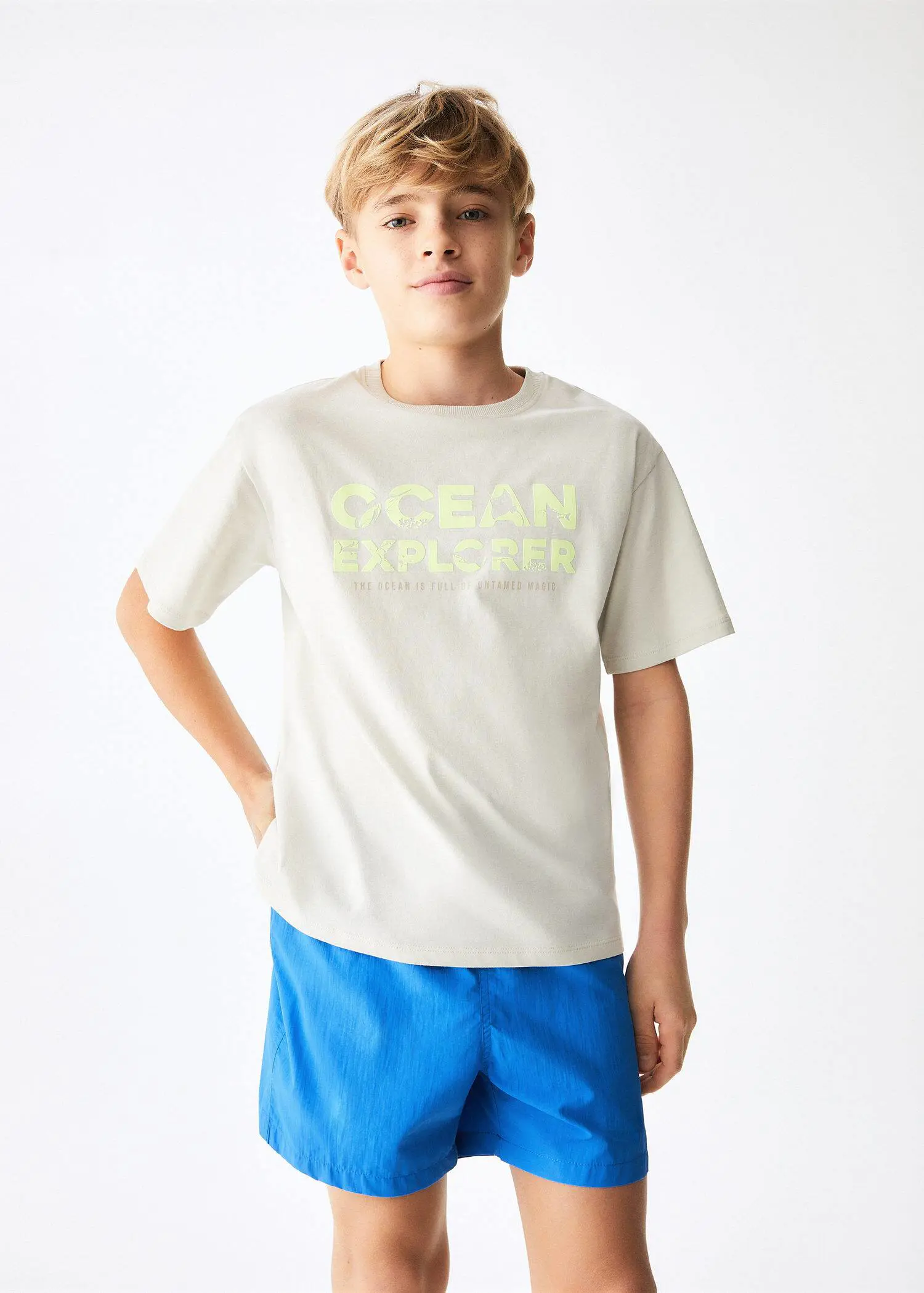Mango KIDS/ Bañador básico. a young boy wearing a white t-shirt and blue swim trunks. 