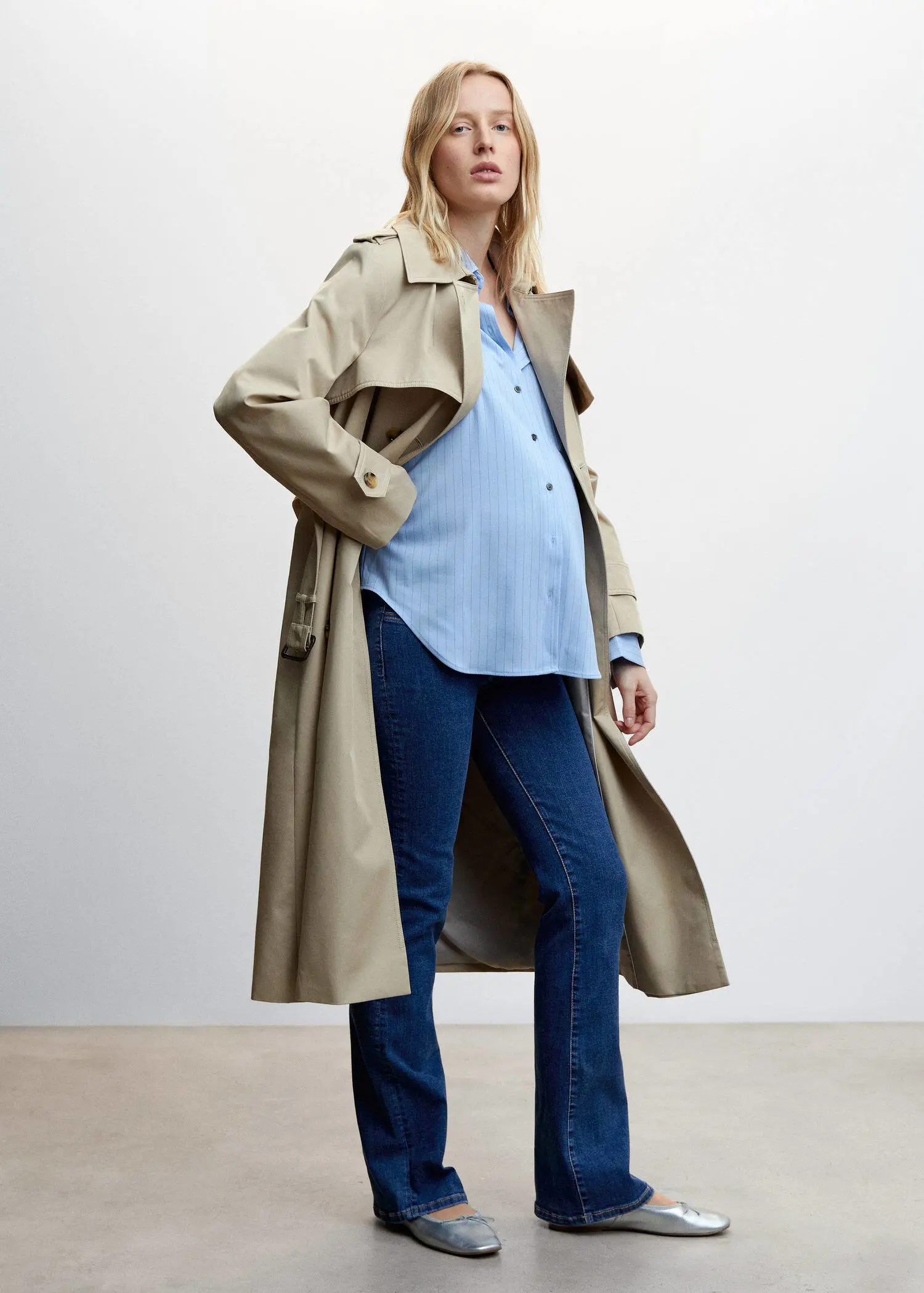 Mango Maternity flared jeans. a woman wearing a trench coat standing in front of a wall. 