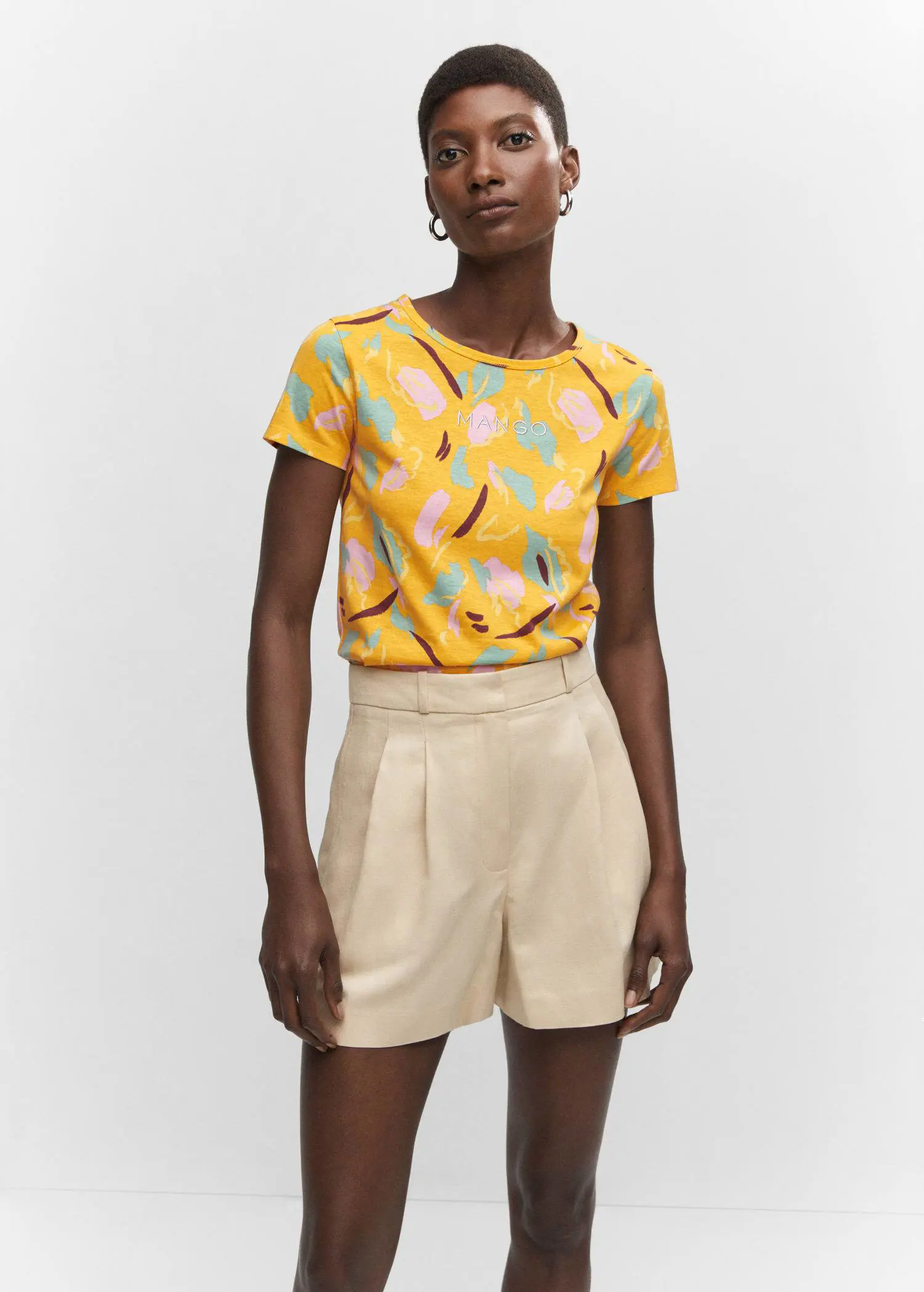 Mango Embroidered logo print t-shirt. a person wearing a yellow shirt and beige shorts. 