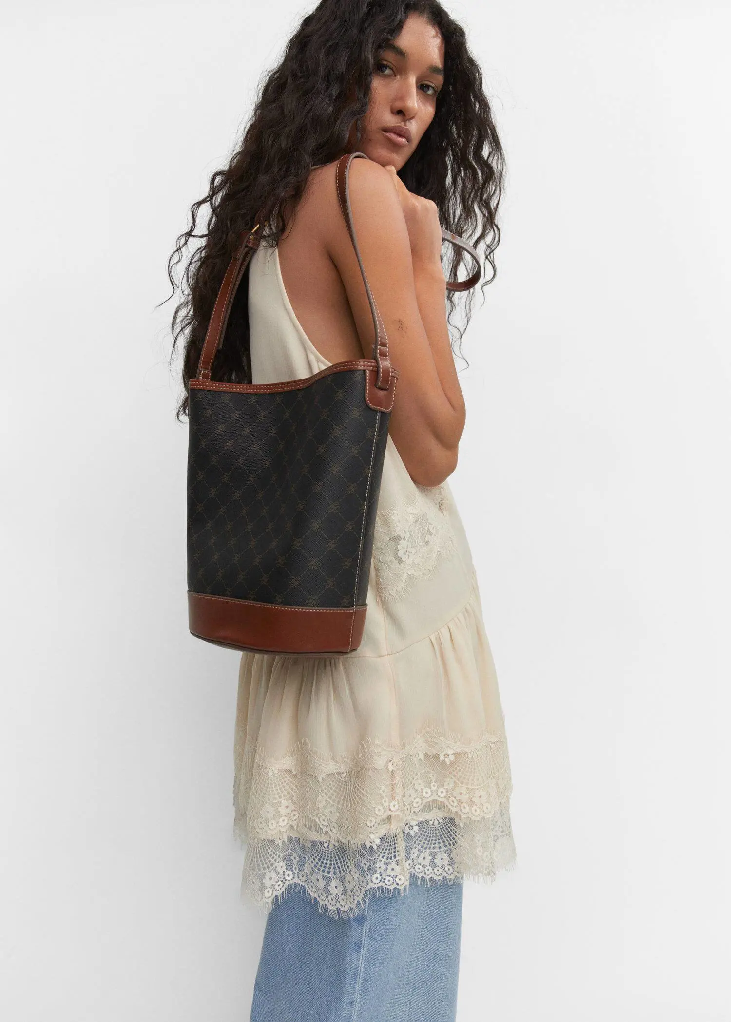 Mango Bucket bag with printed logo. a woman in a white dress holding a black purse. 