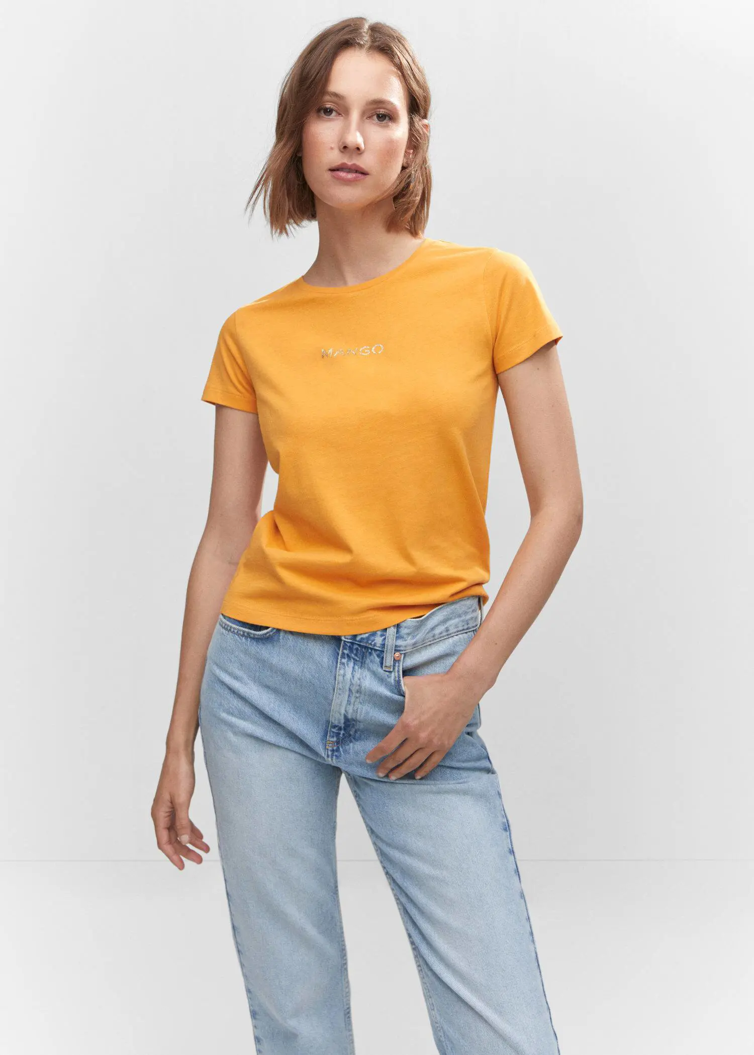 Mango Metallic logo T-shirt. a woman in a yellow t-shirt and jeans. 