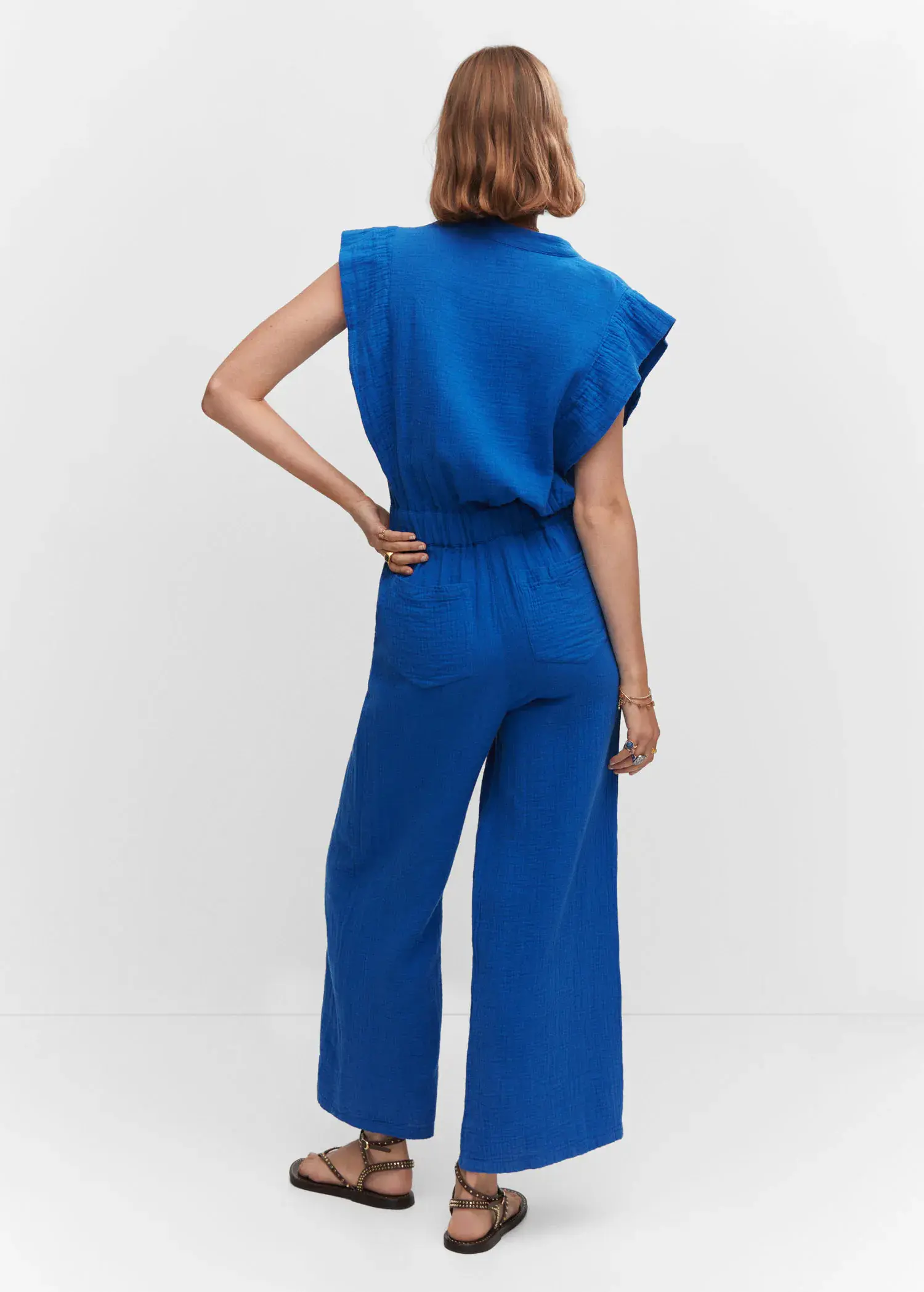 Mango Textured jumpsuit with button. a woman in a blue outfit standing in front of a white wall. 