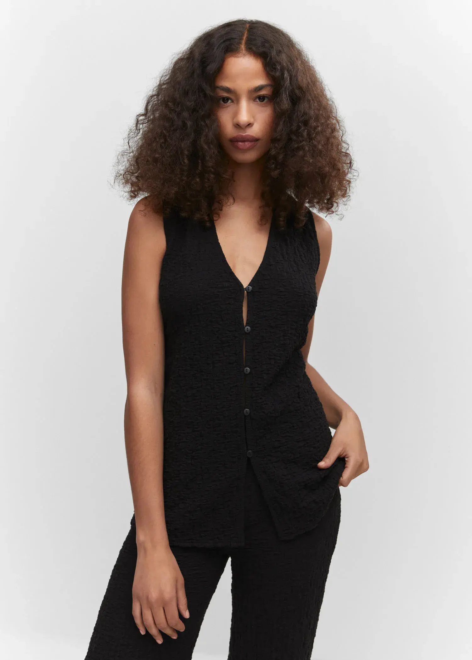 Mango Textured polo neck gilet. a woman in a black outfit with curly hair. 