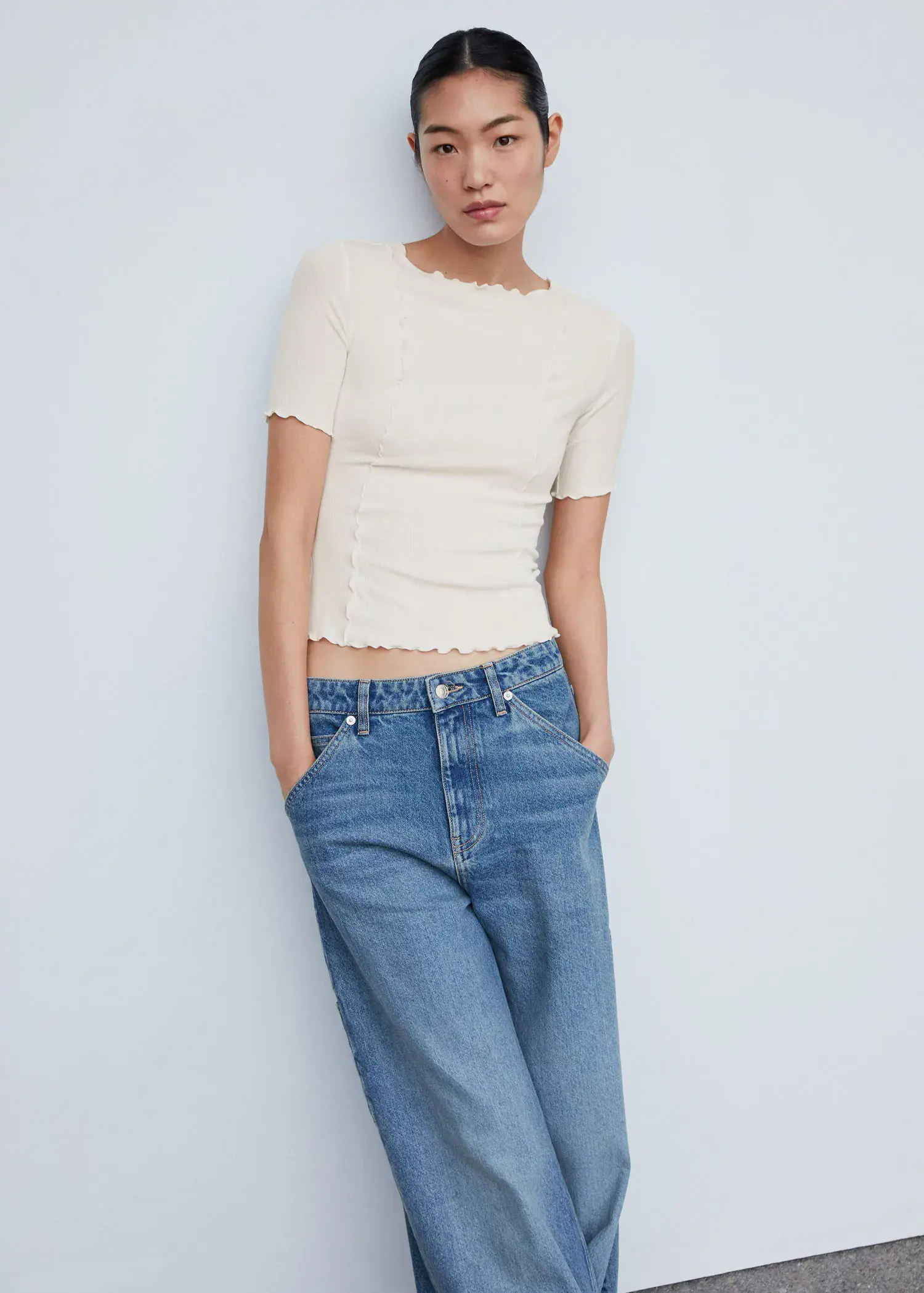 Mango Decorative seam T-shirt. a woman in white shirt and jeans leaning against a wall. 
