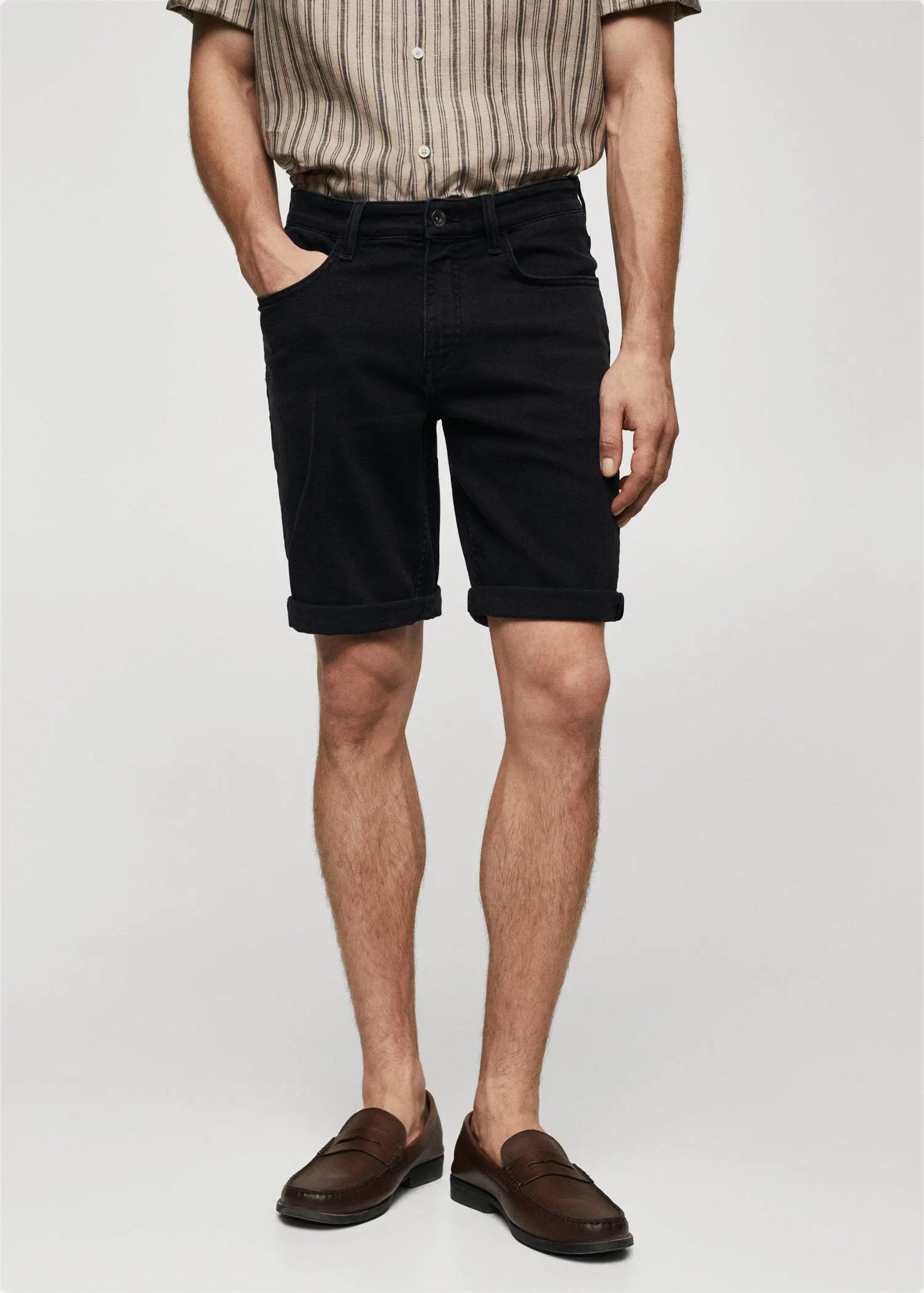 Mango Slim-fit denim bermuda shorts. a man in black shorts is standing up. 