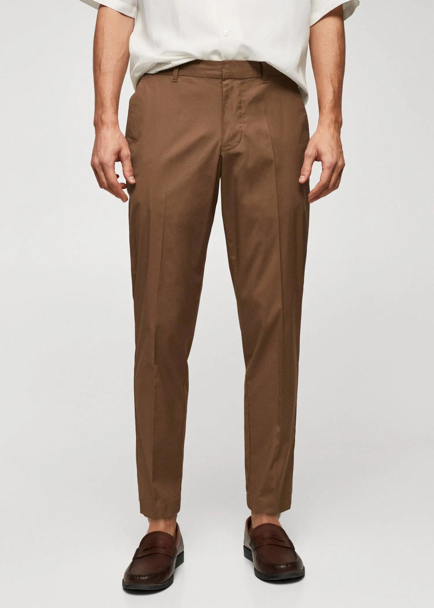 Mango Slim-fit cotton trousers. a man wearing brown pants standing in front of a white wall. 