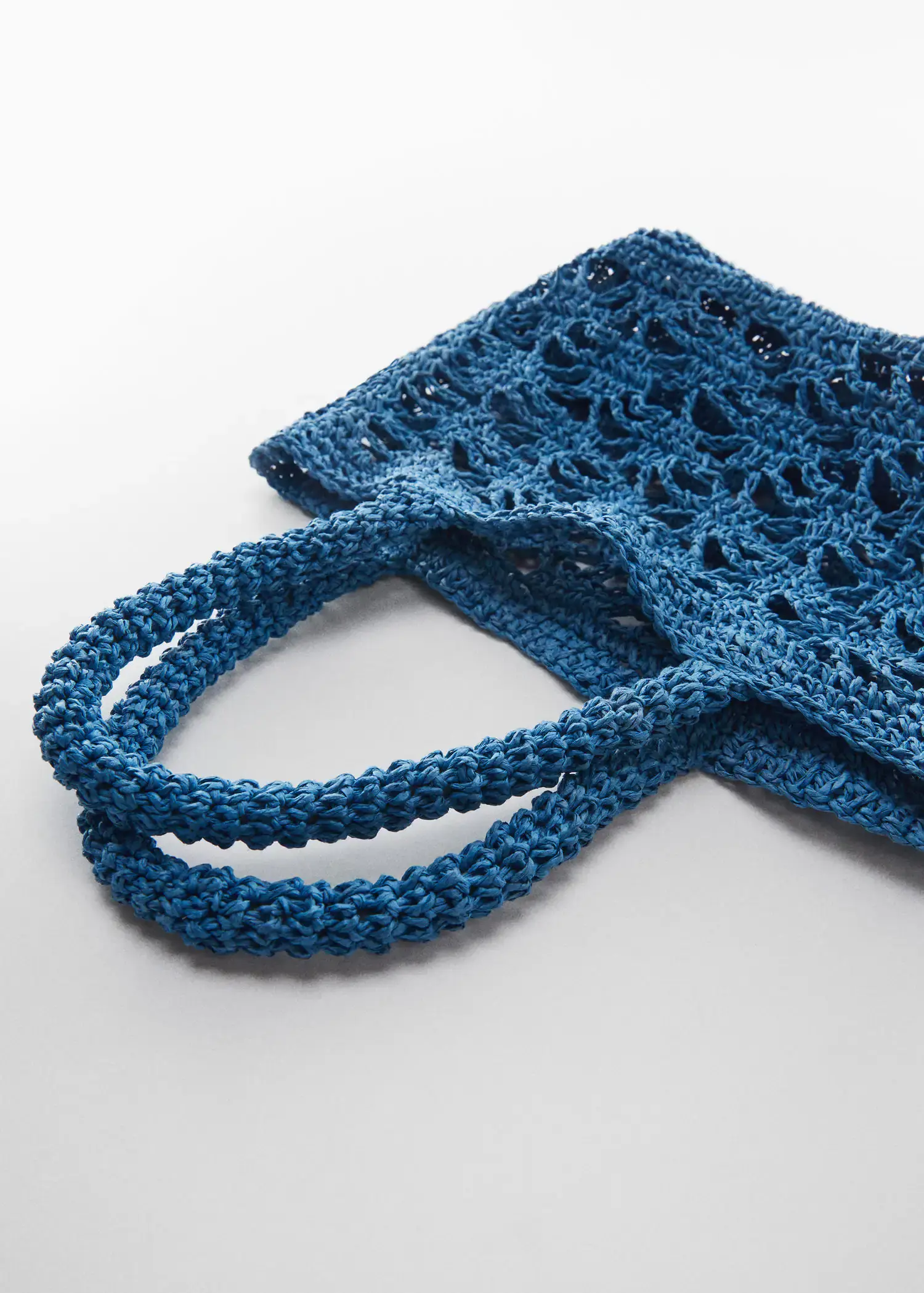 Mango Double-handle raffia bag. a crocheted blue bag is shown on top of a table. 