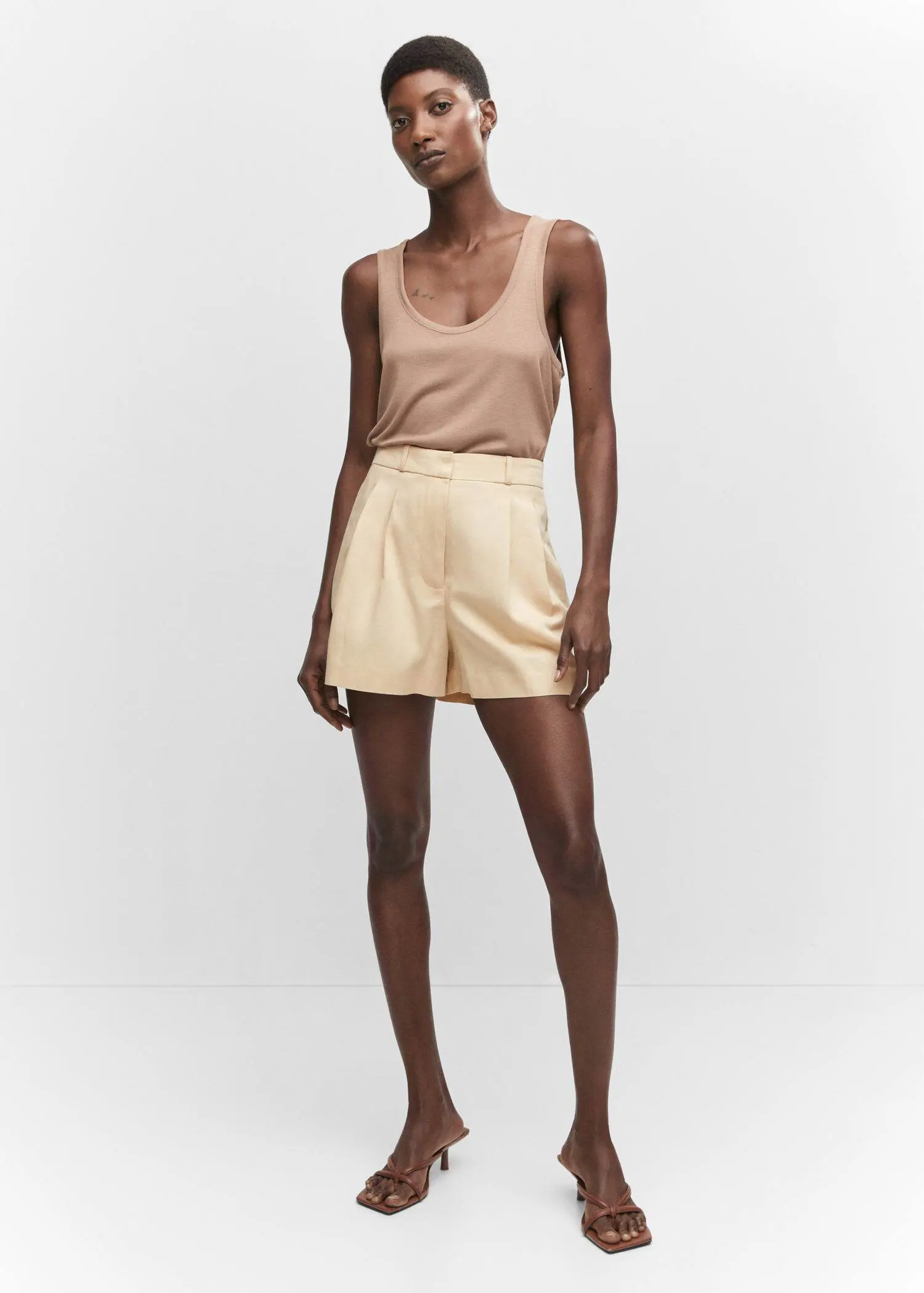 Mango Pleated mid-rise shorts. a woman in a tan tank top and beige shorts. 