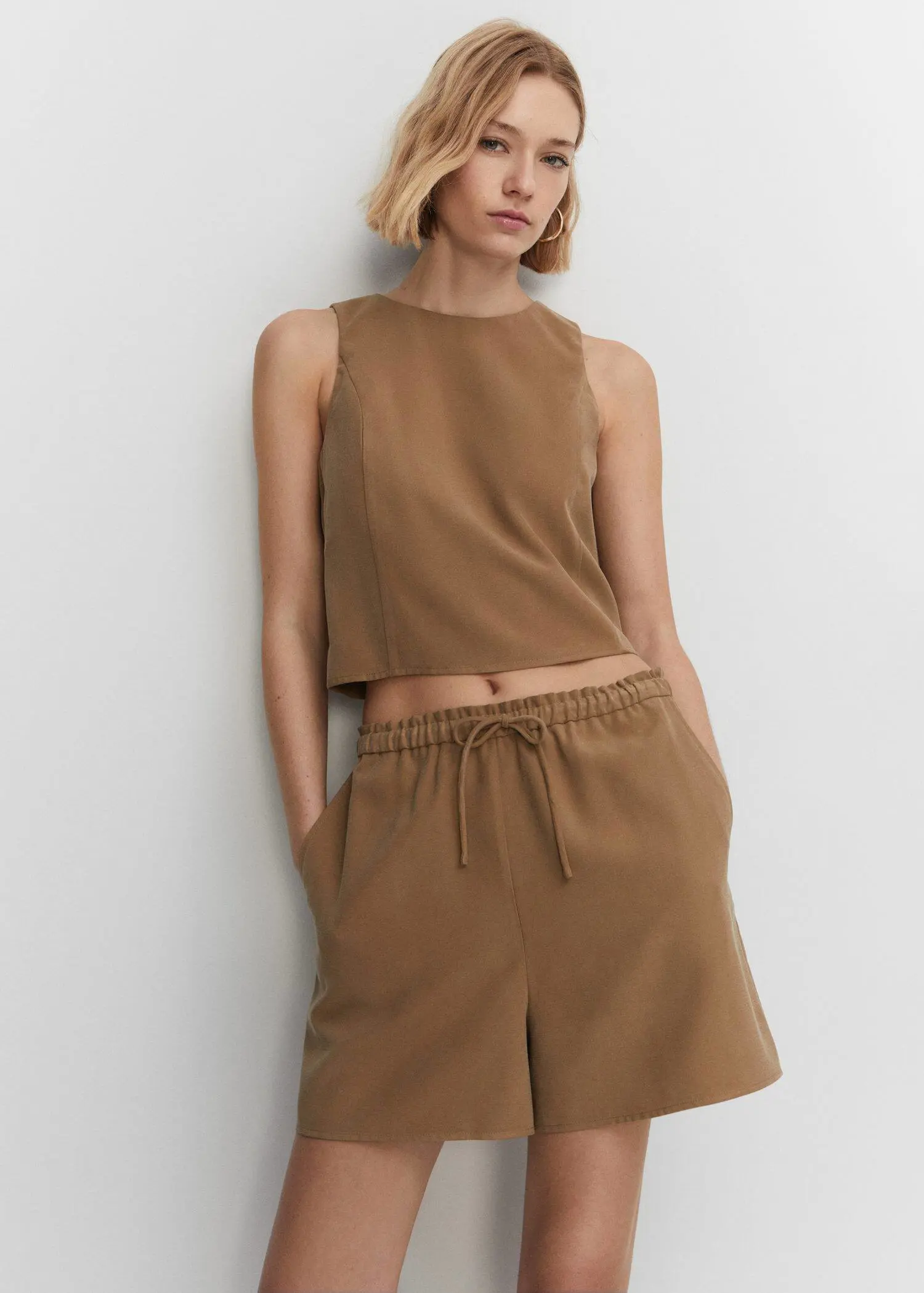 Mango Elastic waist shorts. a woman leaning against a wall wearing a brown outfit. 