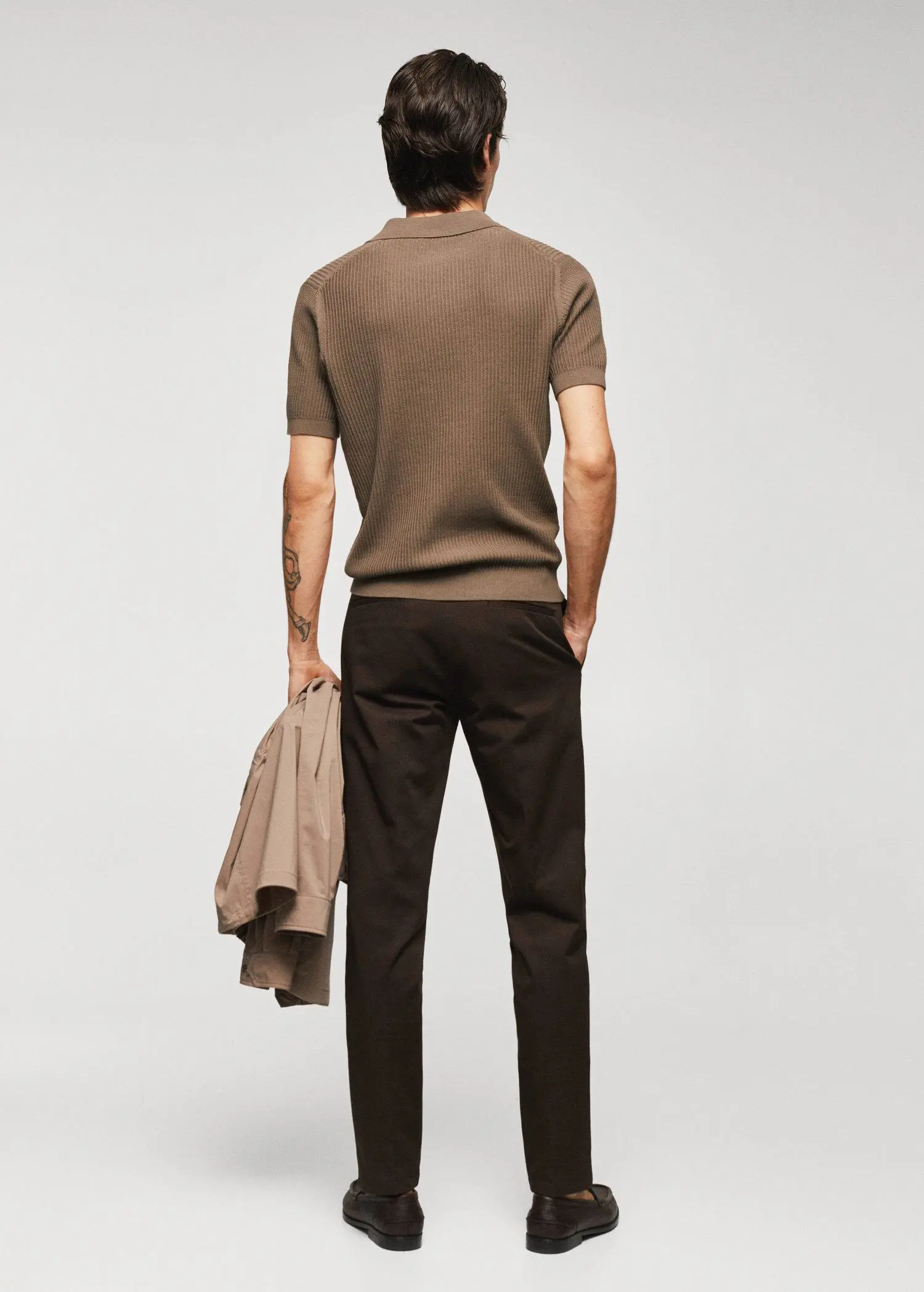 Mango Ribbed cotton polo shirt. a man standing in front of a white wall holding a jacket. 