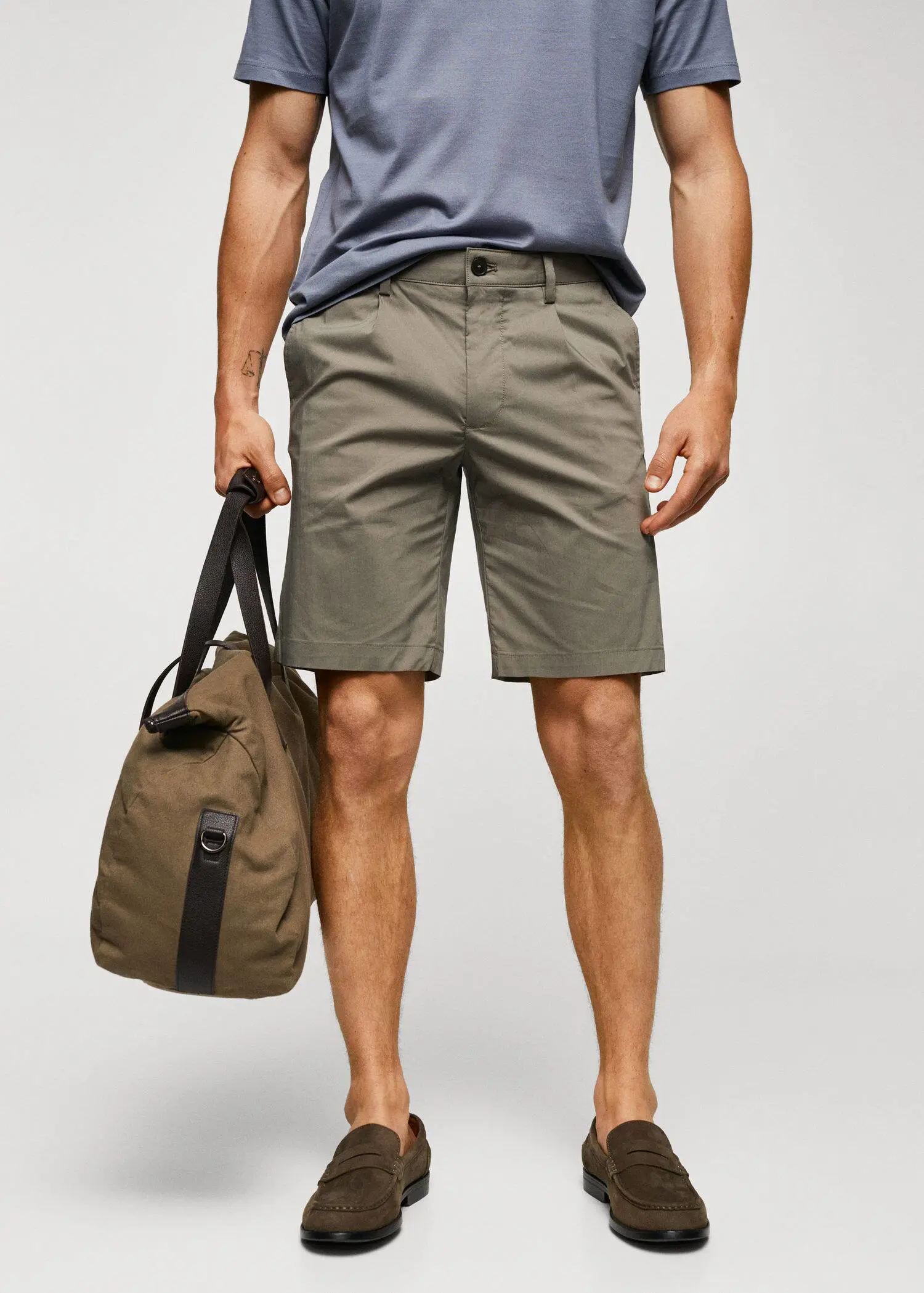 Mango Cotton pleated Bermuda shorts. a man holding a bag while standing in front of a wall. 