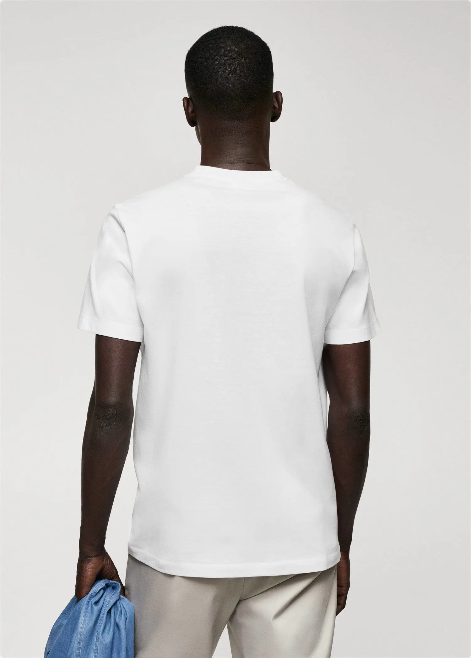 Mango Basic cotton V-neck T-shirt. a man in a white shirt is standing in front of a wall 