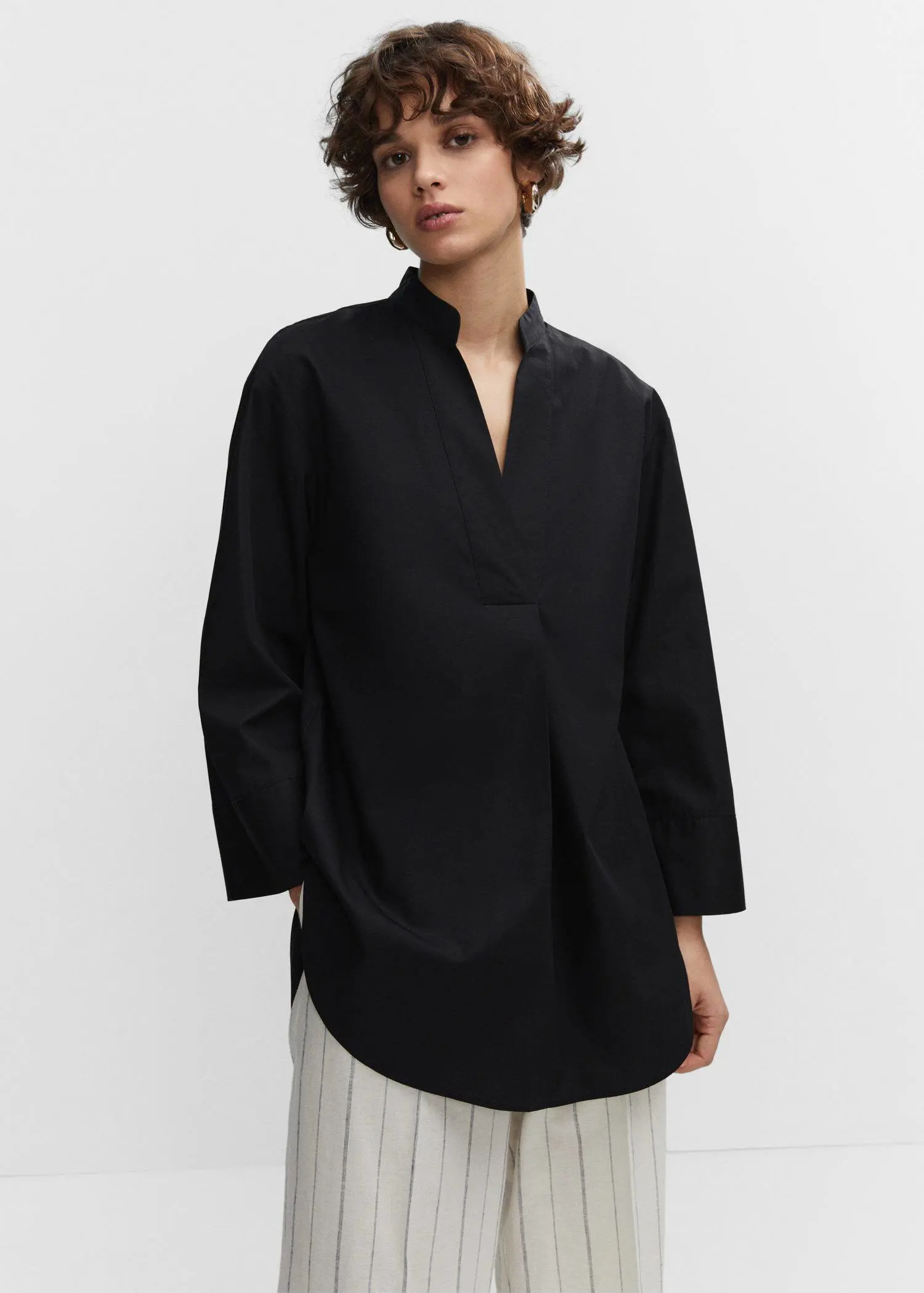 Mango Oversized V-neck blouse. a person wearing a black shirt standing next to a wall 