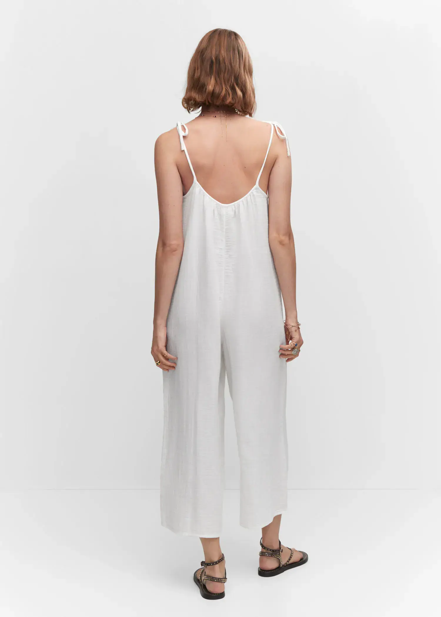 Mango Textured jumpsuit with bows. a woman wearing a white dress standing next to a white wall. 