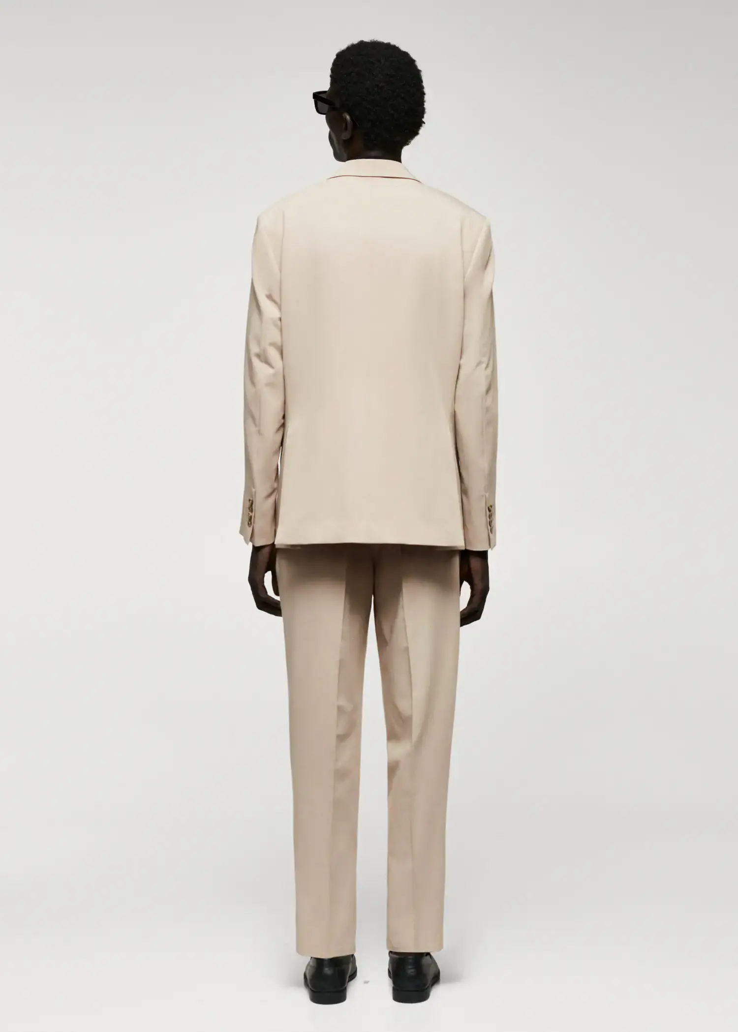 Mango Regular fit suit blazer. a man wearing a suit standing next to a white wall. 