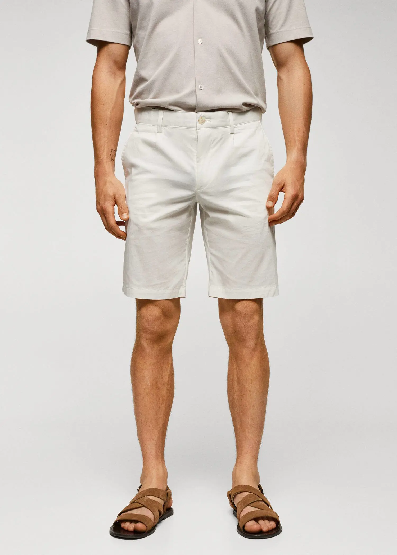 Mango Cotton pleated Bermuda shorts. a man standing in front of a white wall. 