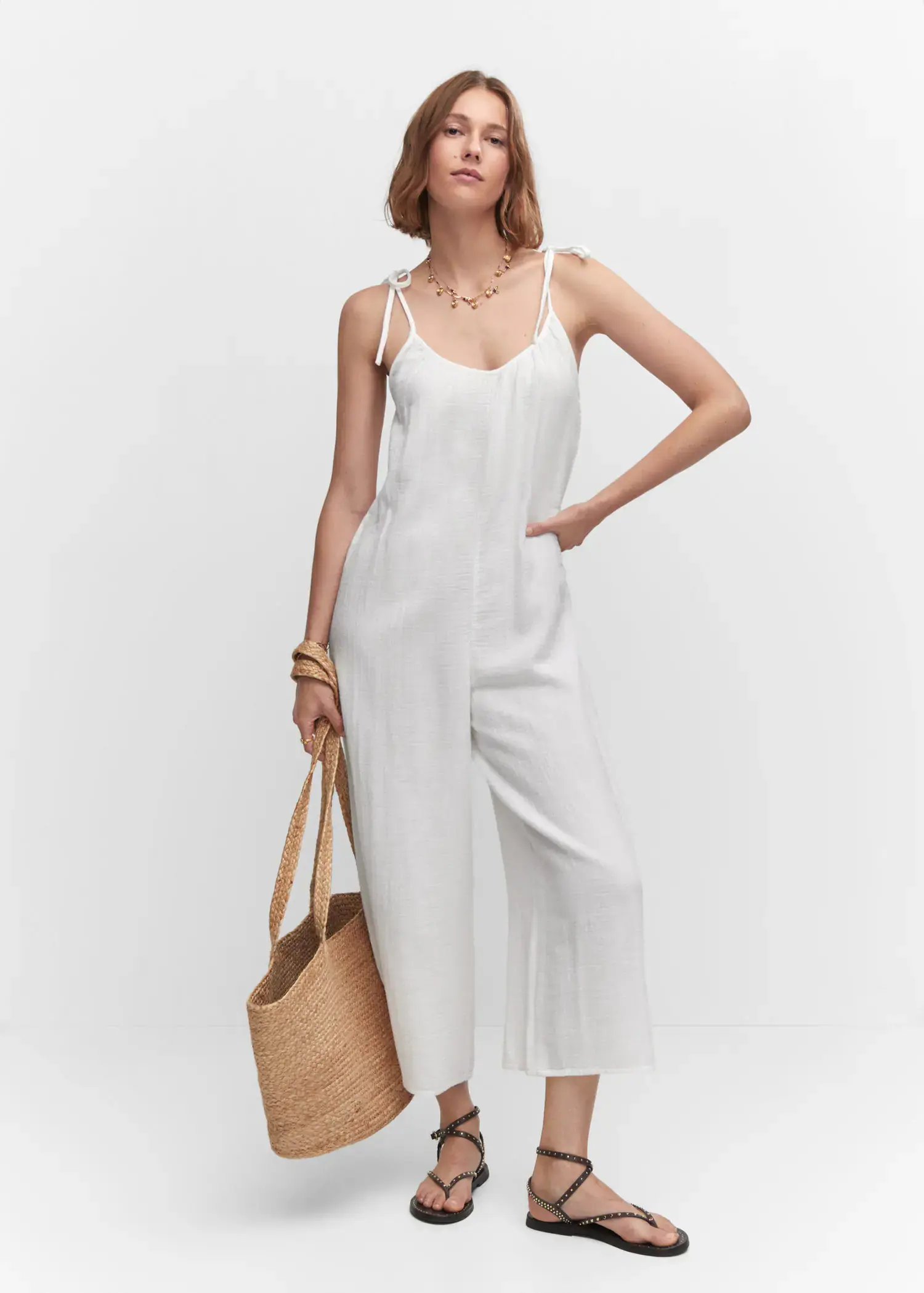 Mango Textured jumpsuit with bows. a woman in a white jumpsuit holding a straw bag. 