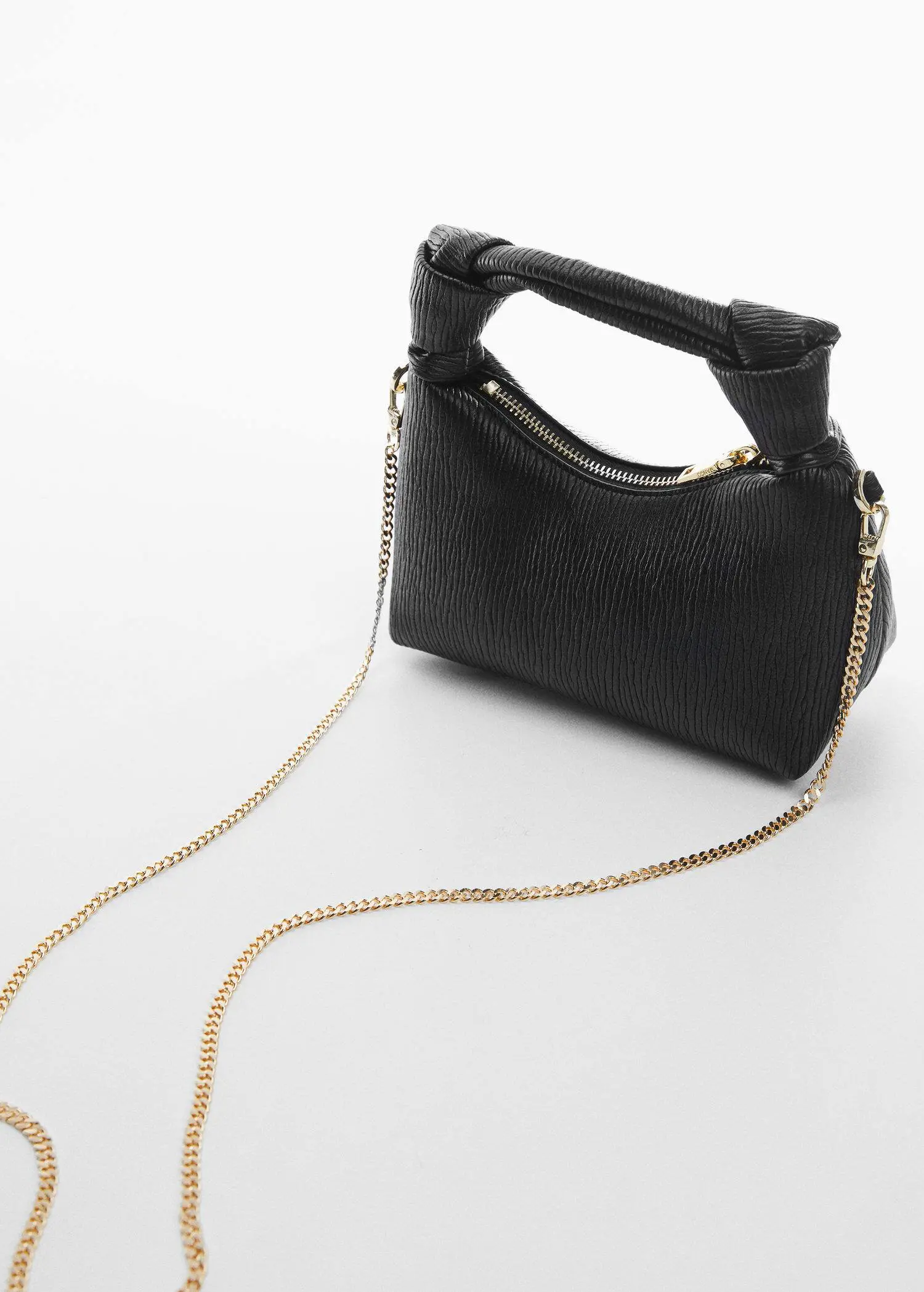 Mango Textured knot handle bag. a black purse with a gold chain on a white surface. 