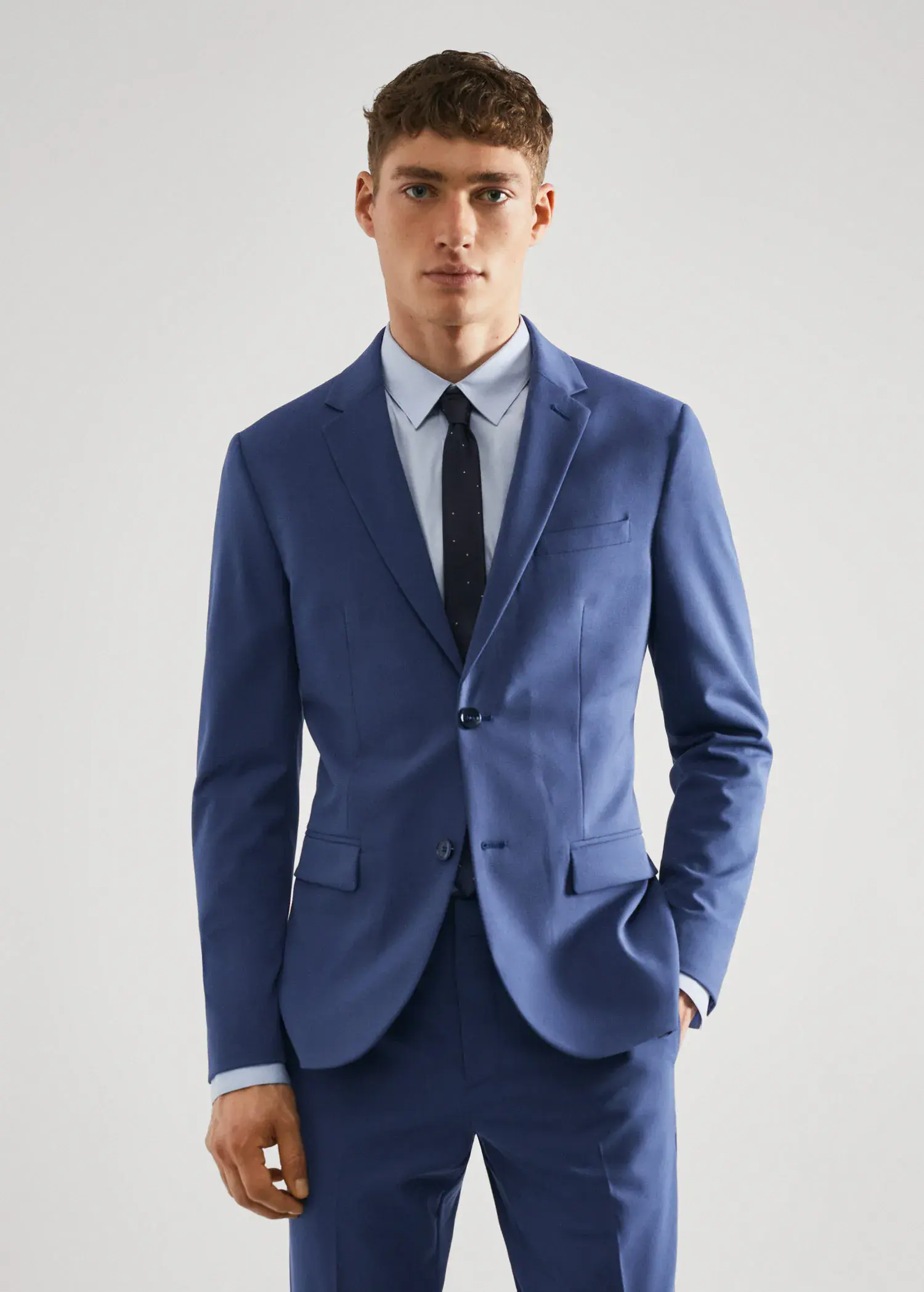 Mango Super slim-fit suit jacket in stretch fabric. a man in a suit and tie standing with his hands in his pockets. 