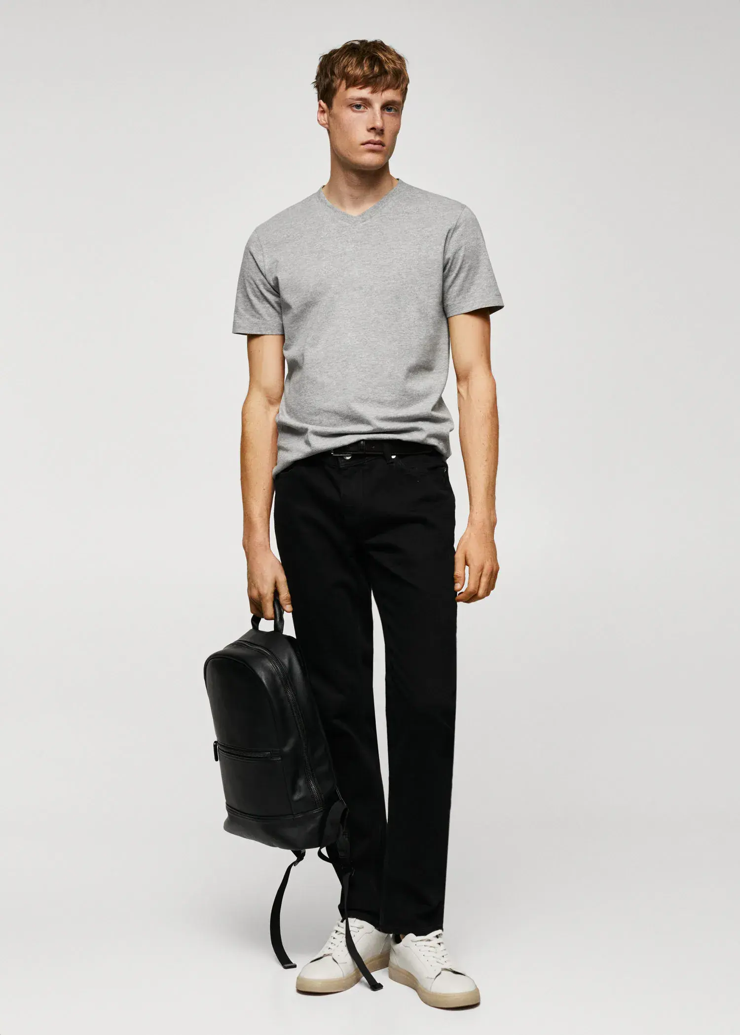 Mango Basic cotton V-neck T-shirt. a young man holding a backpack in front of a white wall. 