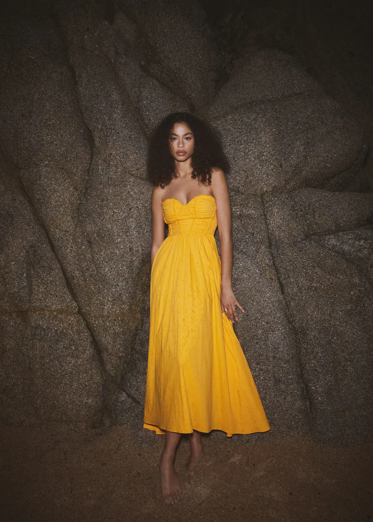 Mango Flared corset dress. a woman in a yellow dress standing in front of a rock wall. 