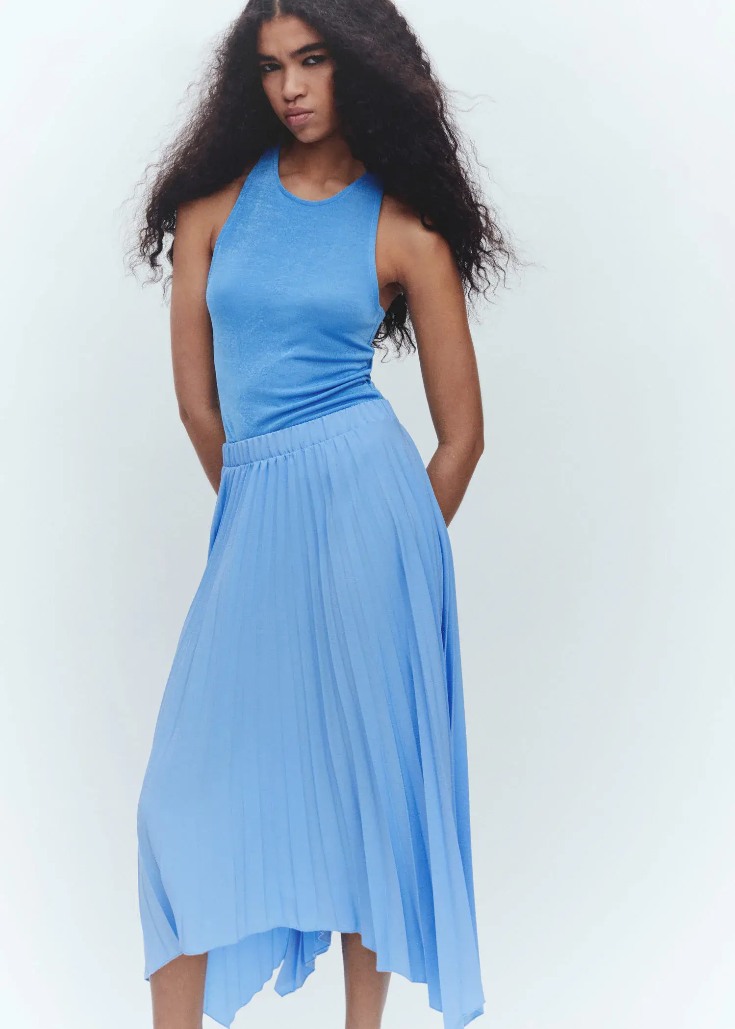 Mango Pleated asymmetric skirt . a woman standing in a blue dress with her hands in her pockets 