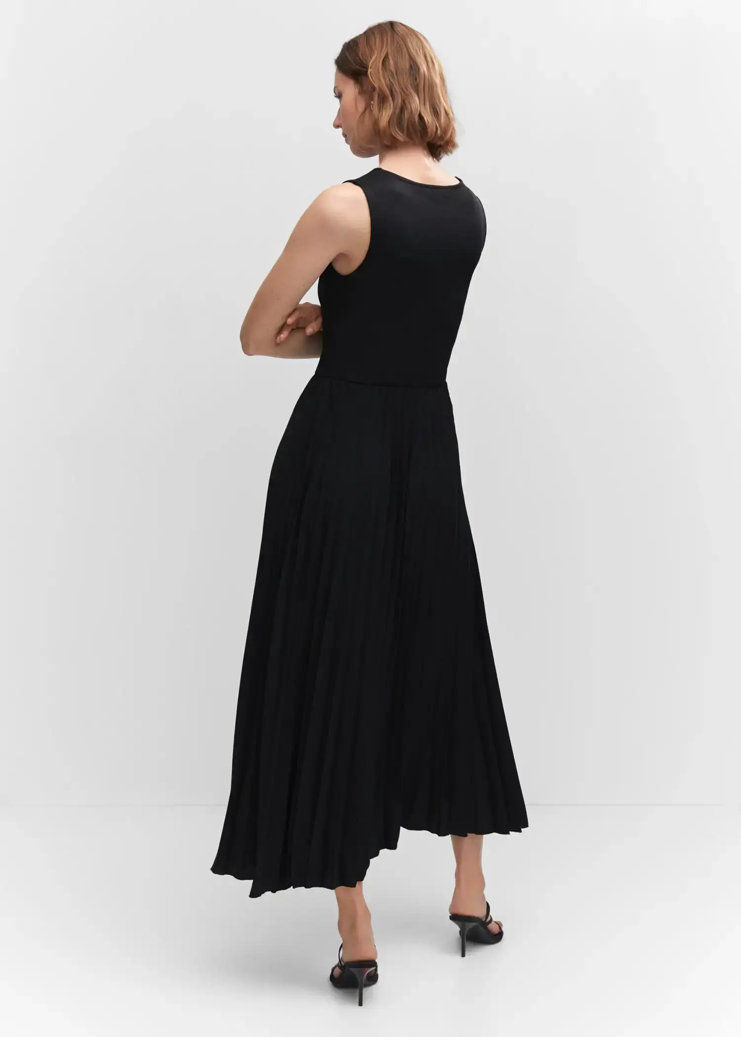 Mango Pleated hem dress. a woman wearing a black dress standing in a room. 