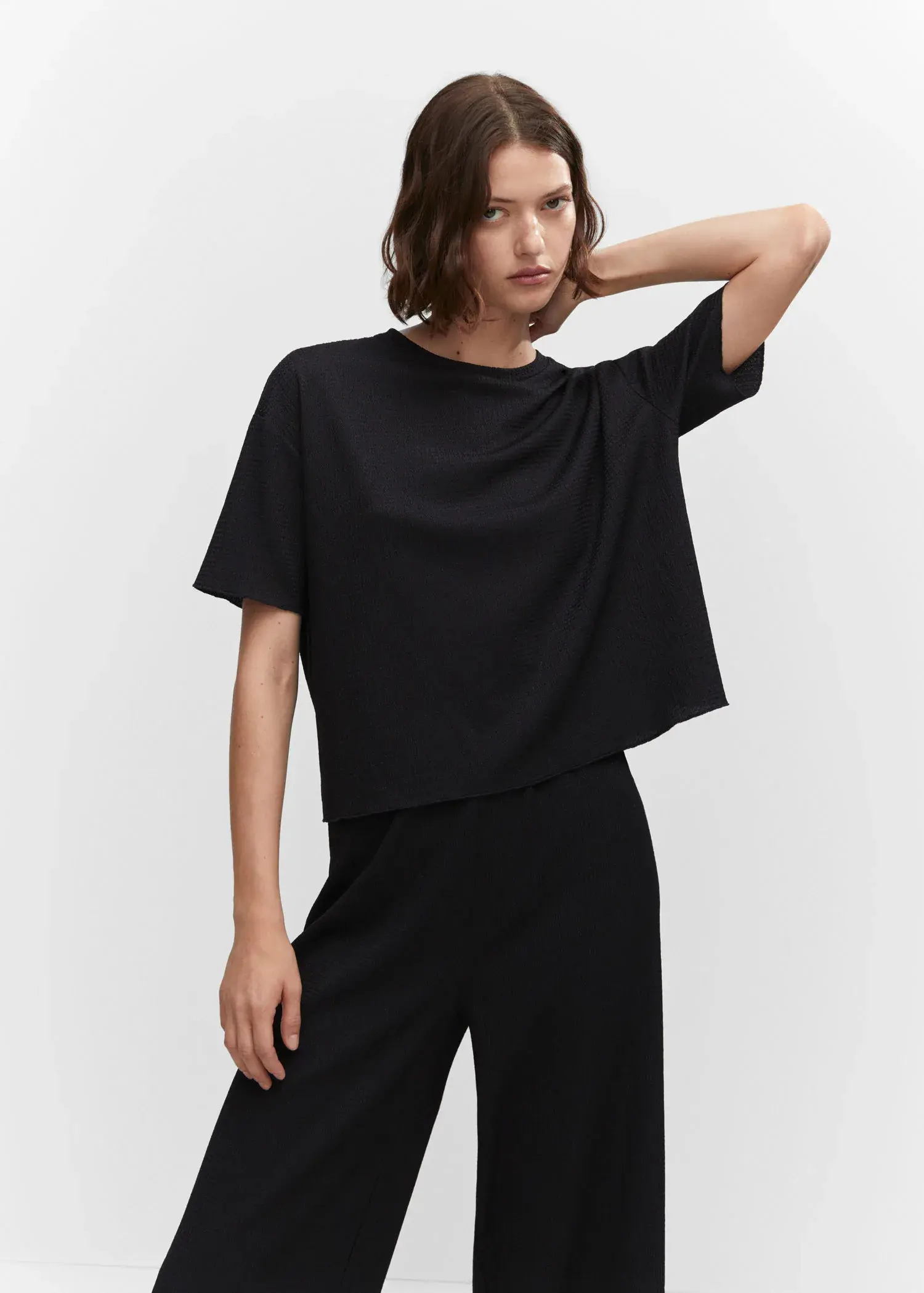Mango Oversized textured t-shirt. a woman wearing a black top and black pants. 