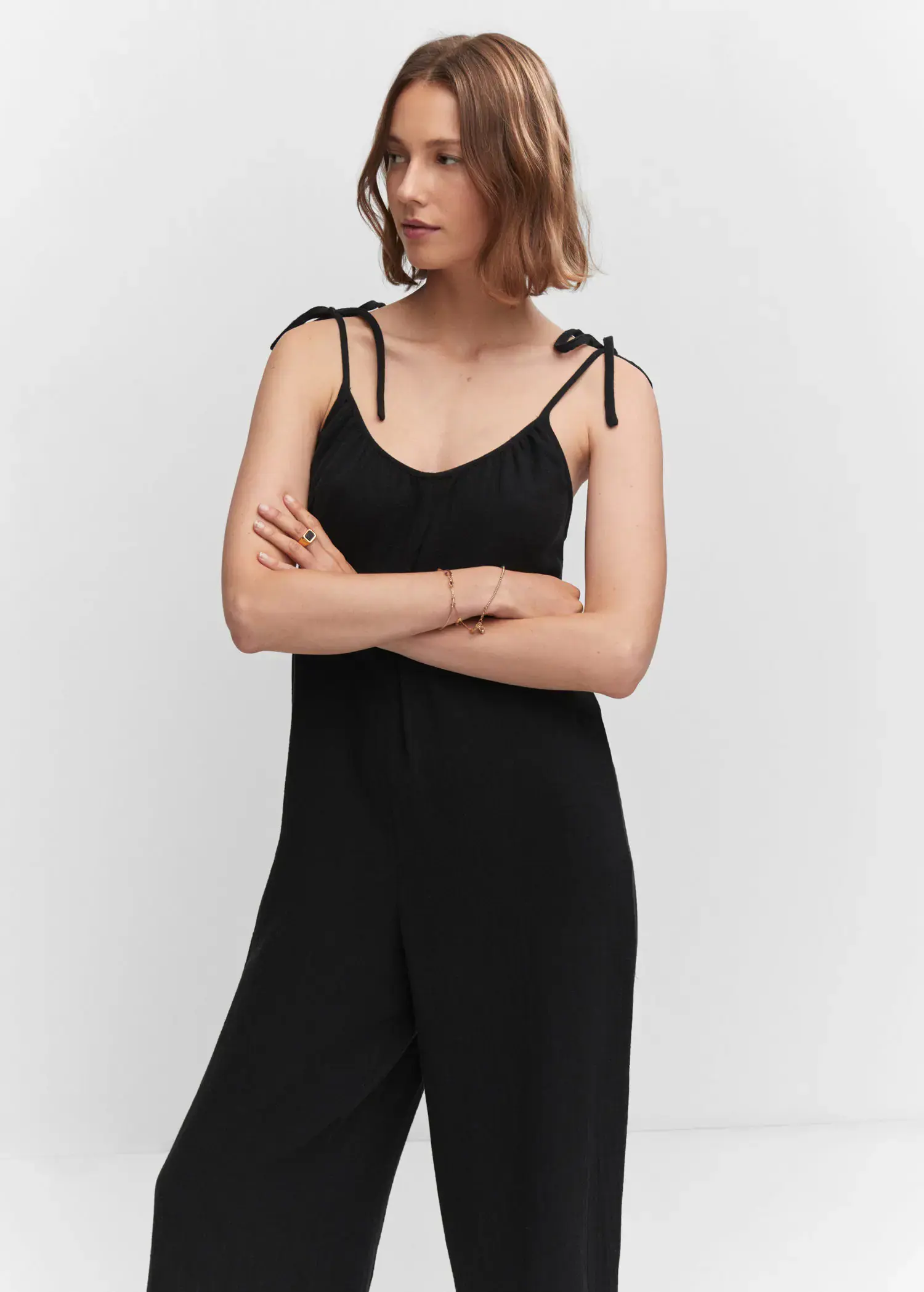 Mango Textured jumpsuit with bows. a woman in a black jumpsuit with her arms crossed. 