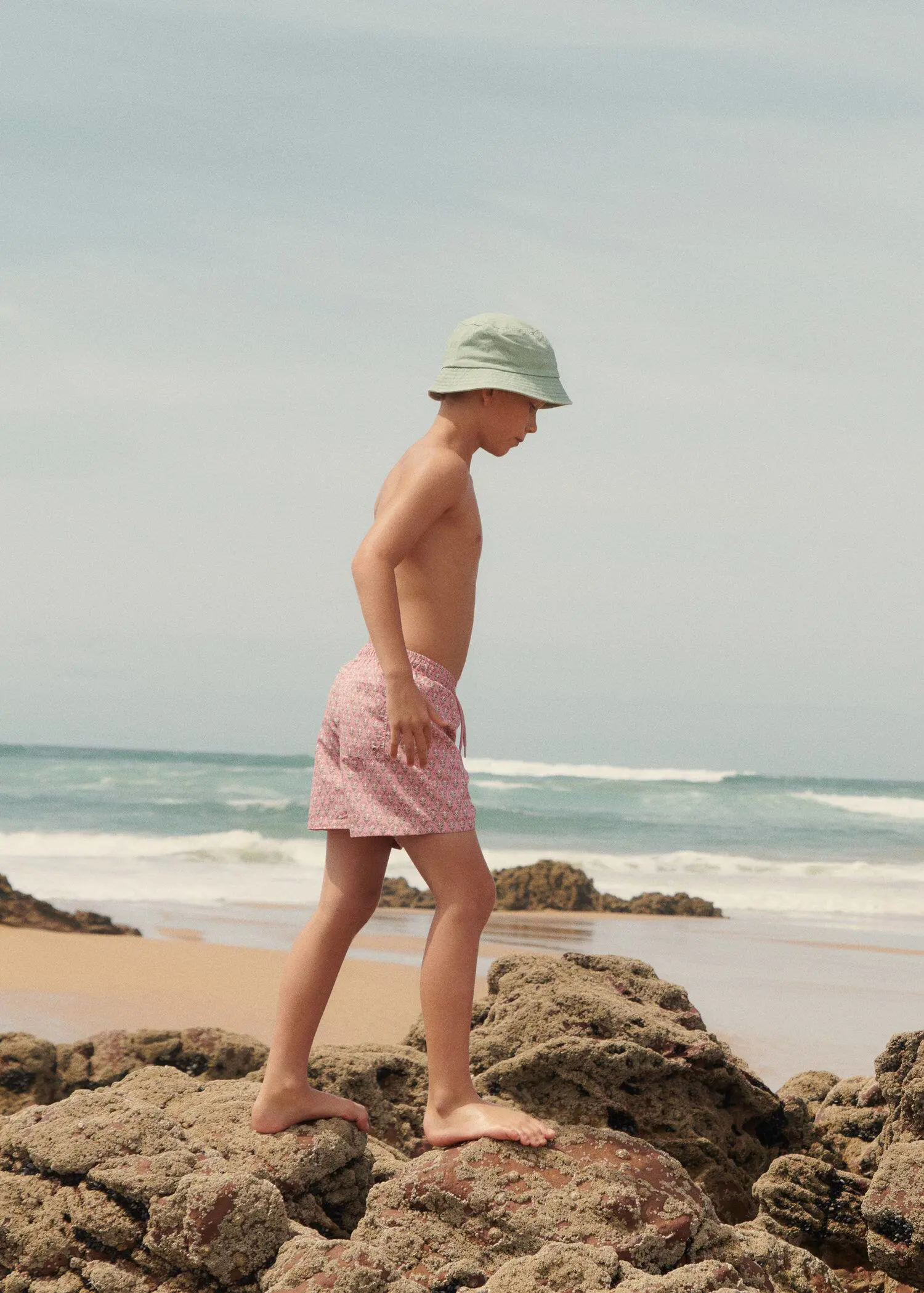 Mango KIDS/ Floral print swimsuit. a man walking on the beach wearing a hat. 