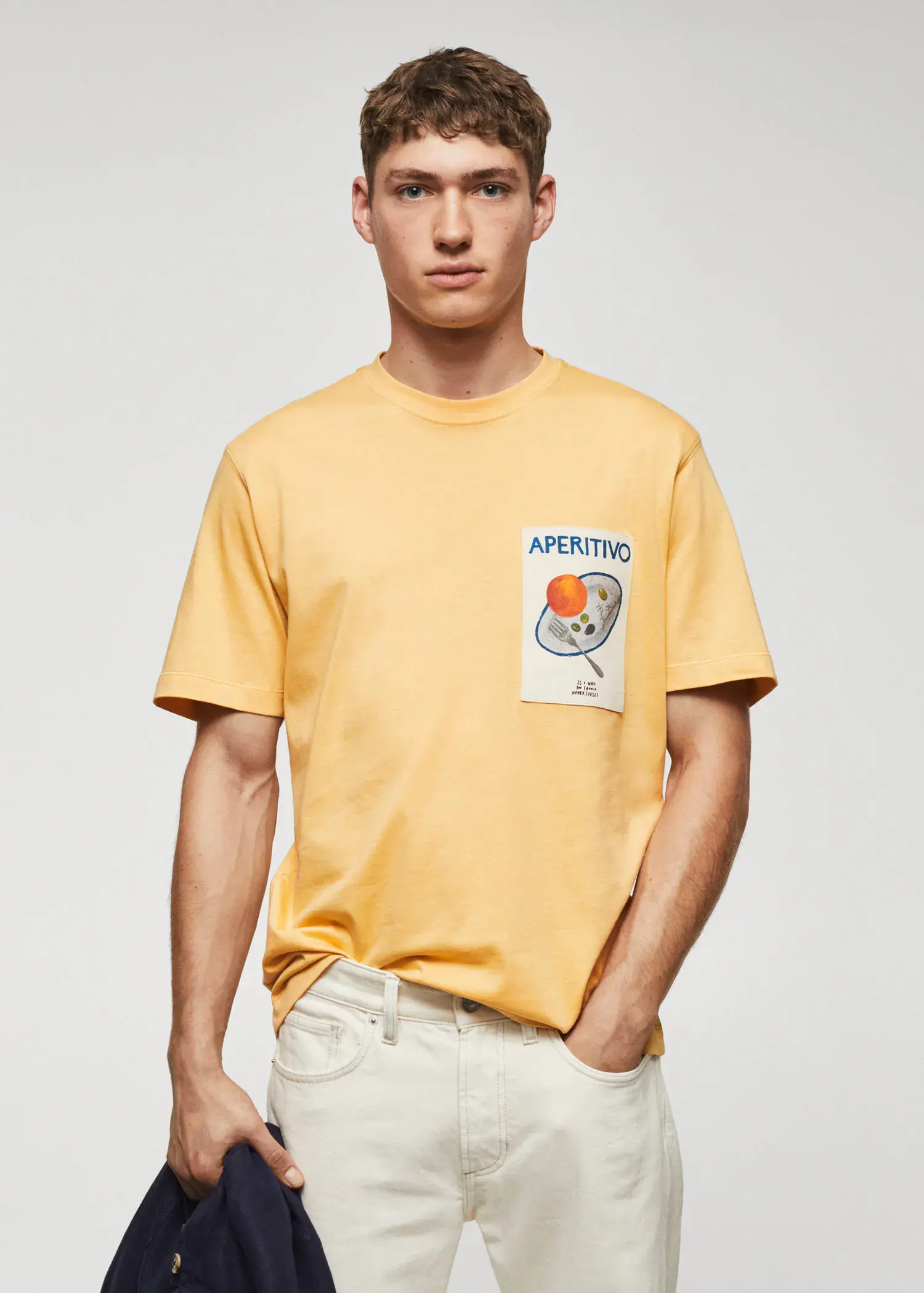 Mango Adriana Eskenazi x Mango t-shirt. a man in a yellow t-shirt is wearing white pants. 