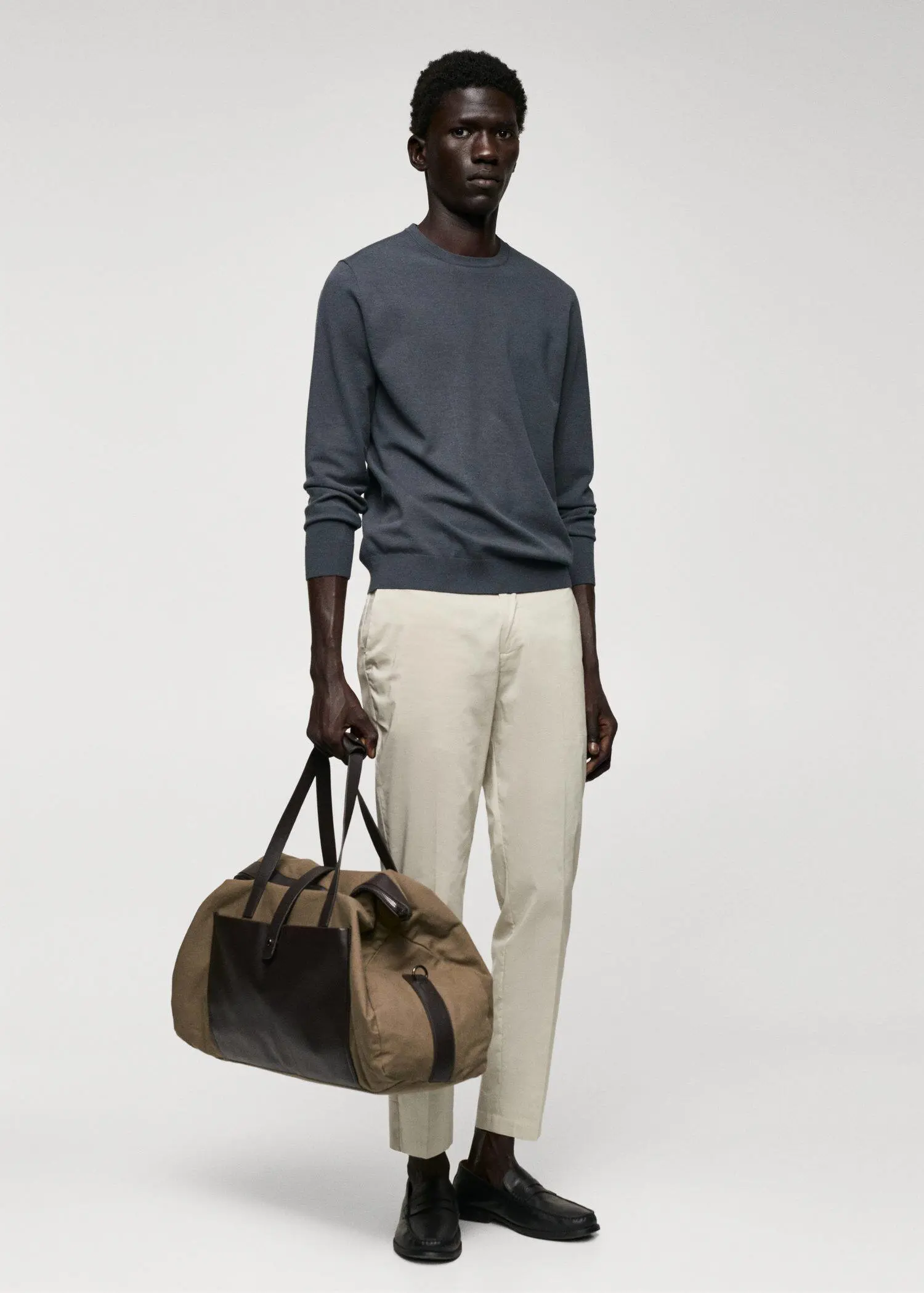 Mango Fine-knit sweater. a man holding a duffel bag in front of a white wall. 
