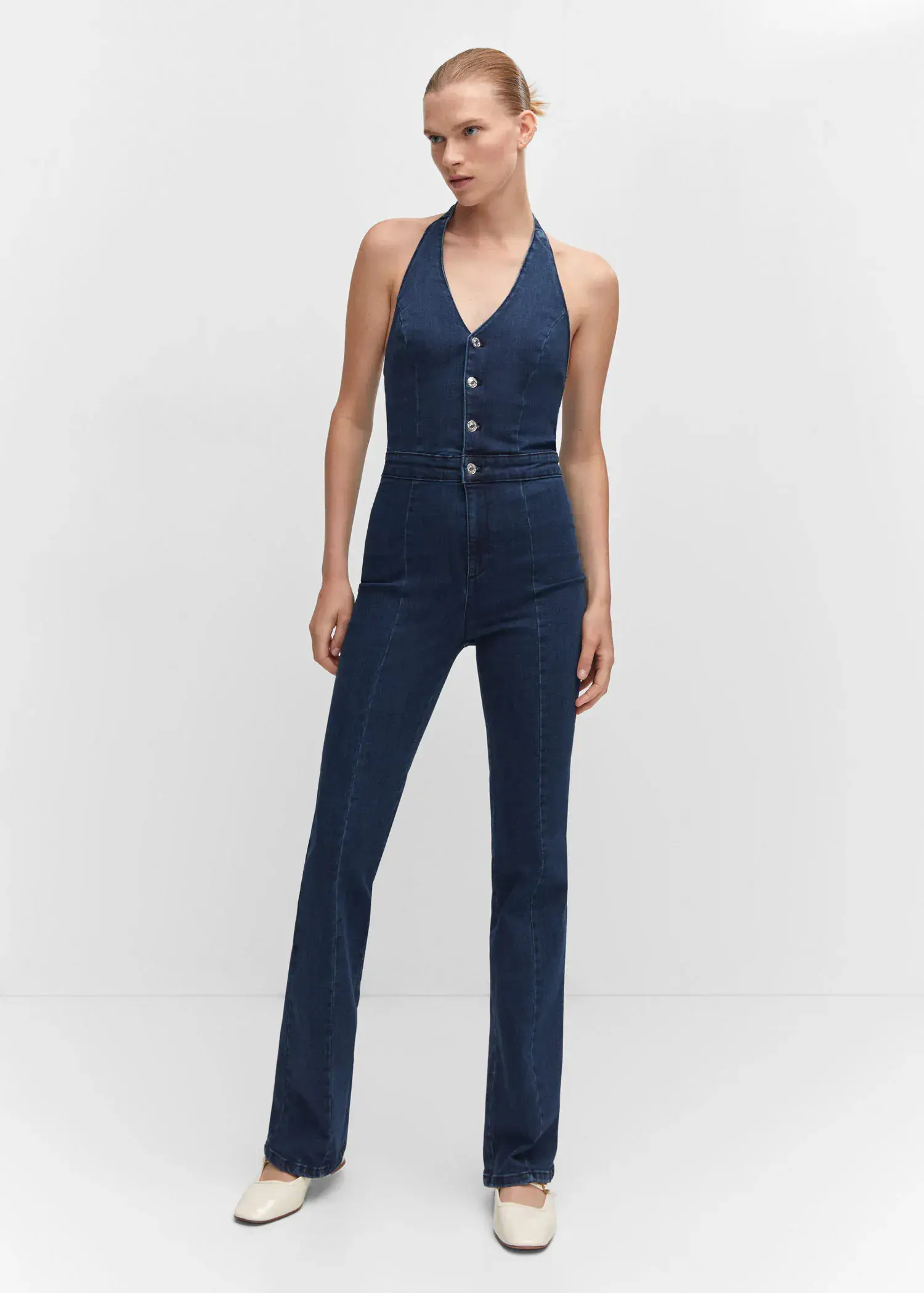 Mango Denim halter-neck jumpsuit. a woman wearing a blue jumpsuit standing in front of a white wall. 