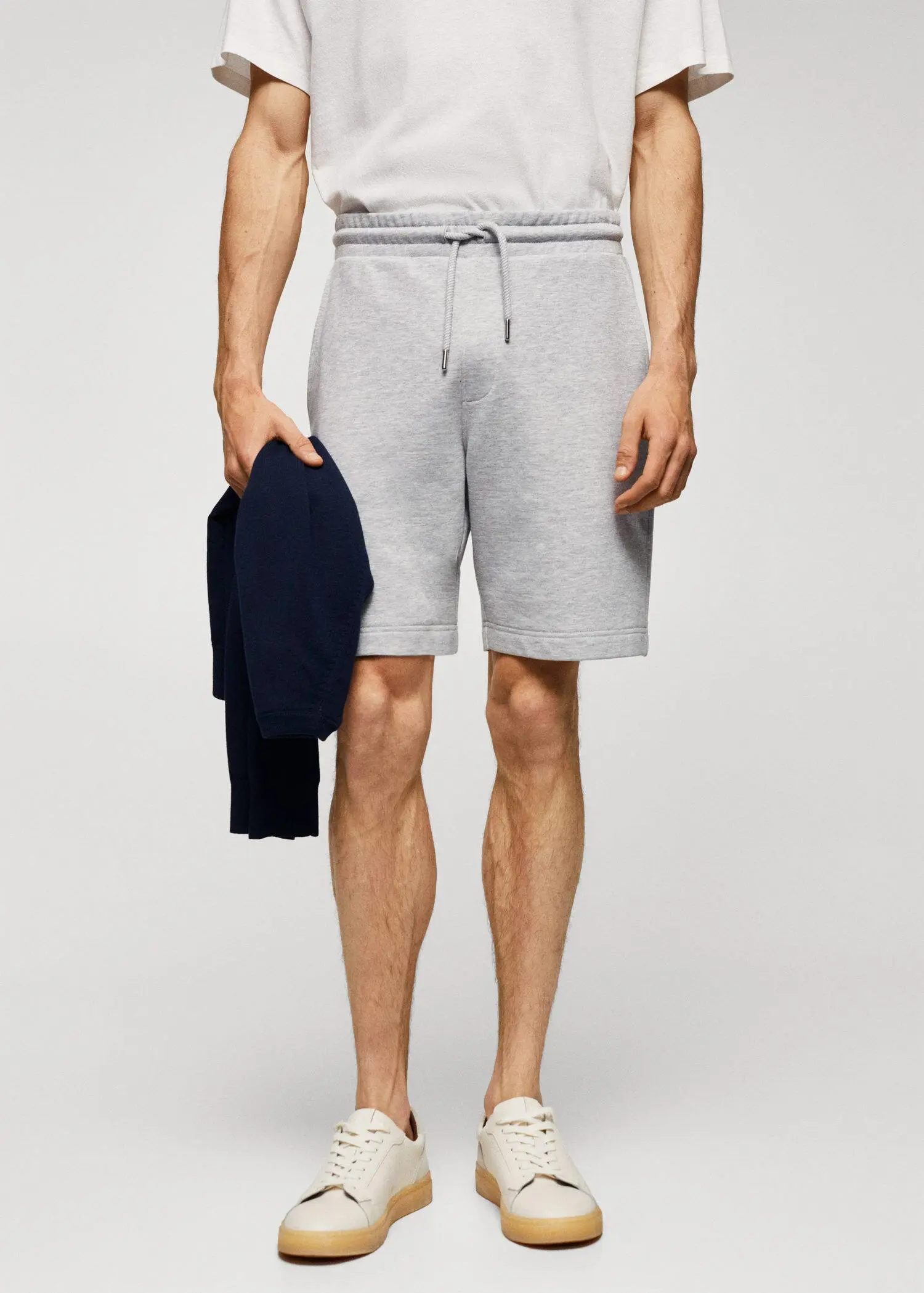 Mango Jogger cotton Bermuda shorts. a man holding a jacket and wearing a pair of shorts. 