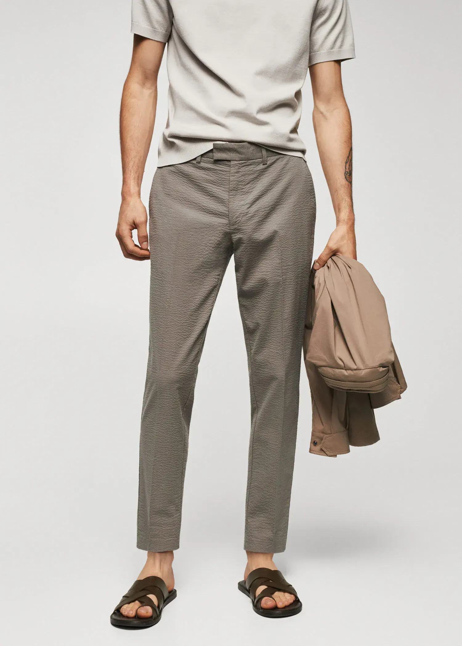 Mango Slim-fit seersucker stretch trousers. a man holding a backpack while standing in front of a wall. 