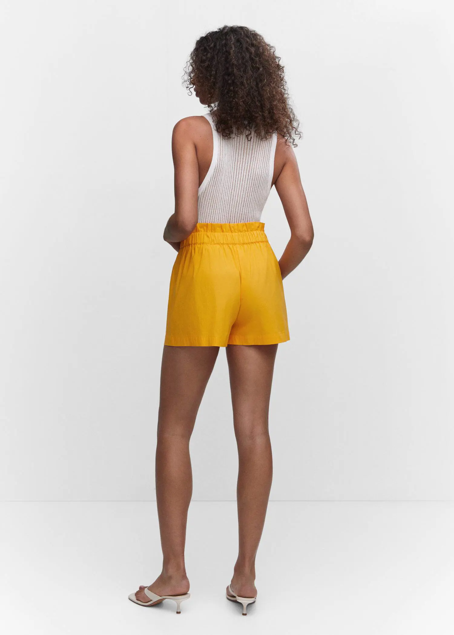 Mango Paperbag shorts with bow. a woman wearing a yellow shorts and a white top. 