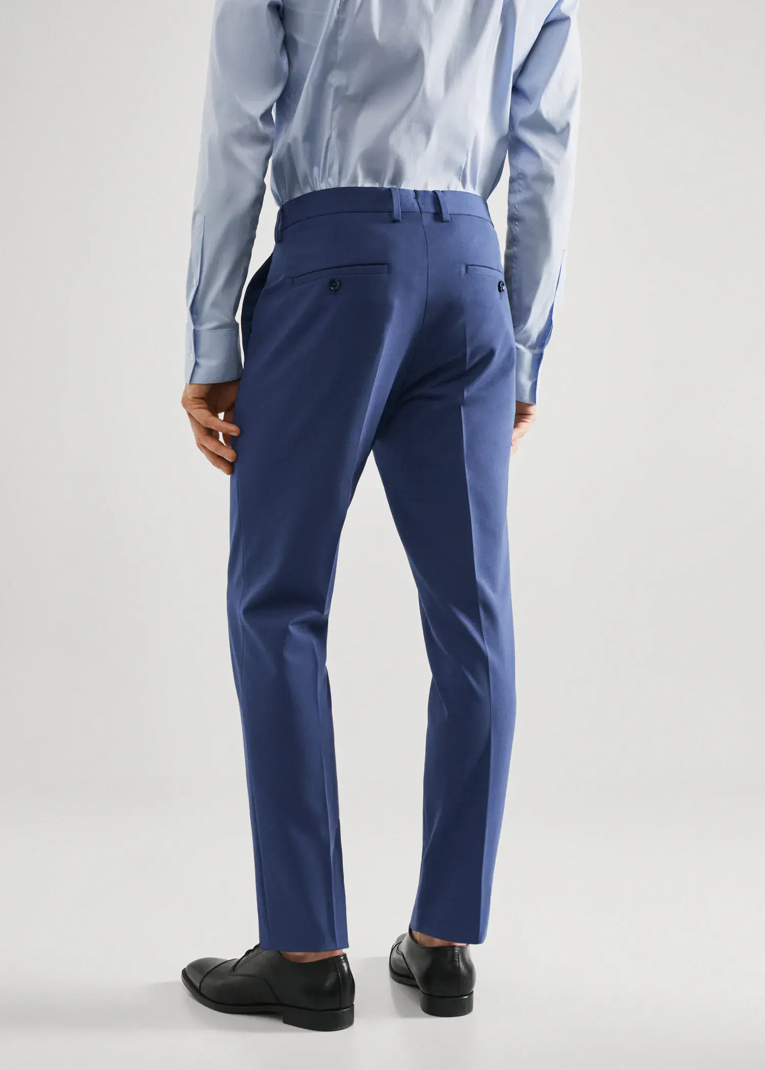 Mango Stretch fabric super slim-fit suit pants. a man wearing a blue suit standing next to a white wall. 